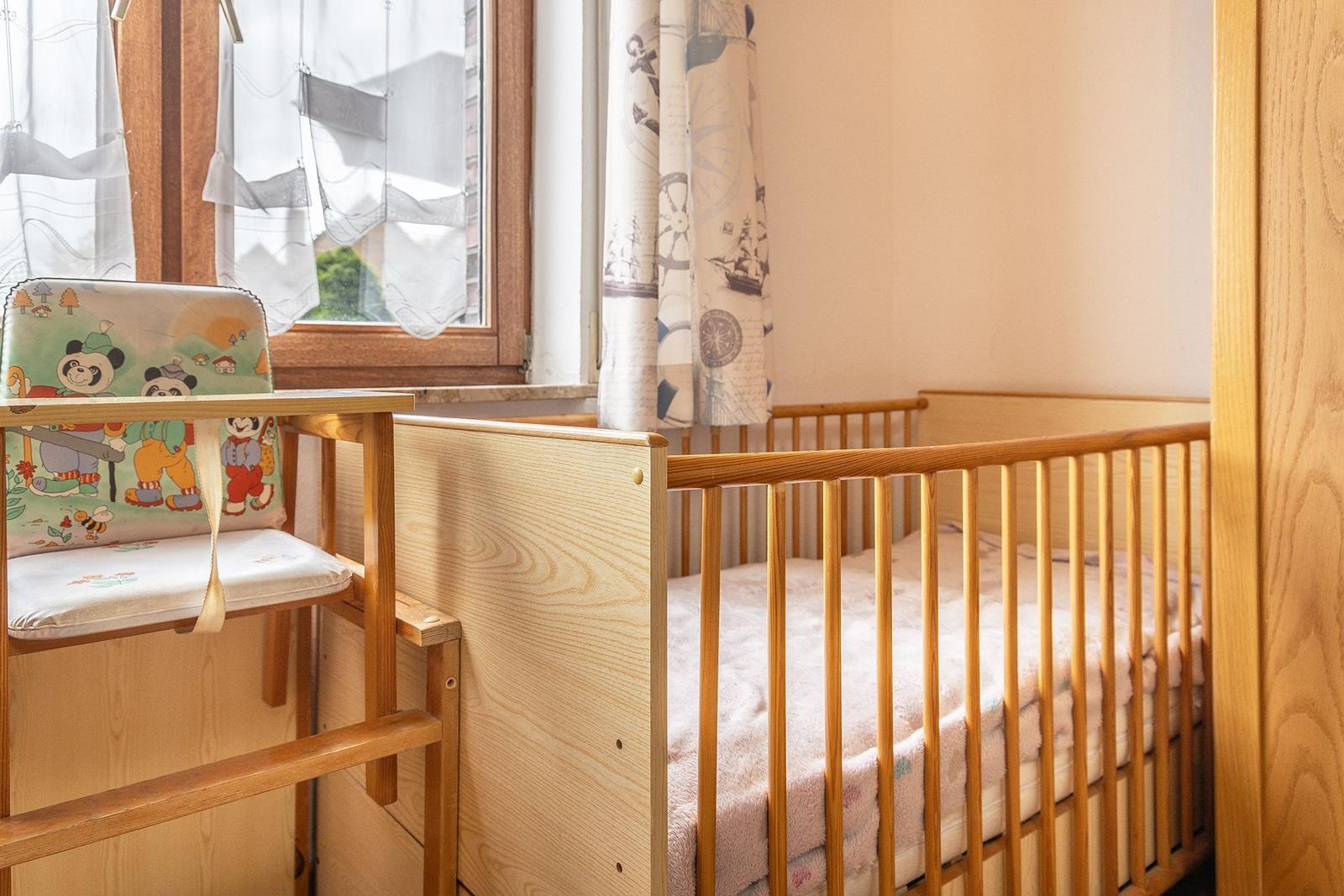 Ein Kinderbett mit Holzgeländer und ein hölzerner Hochstuhl mit Panda-Motiv.