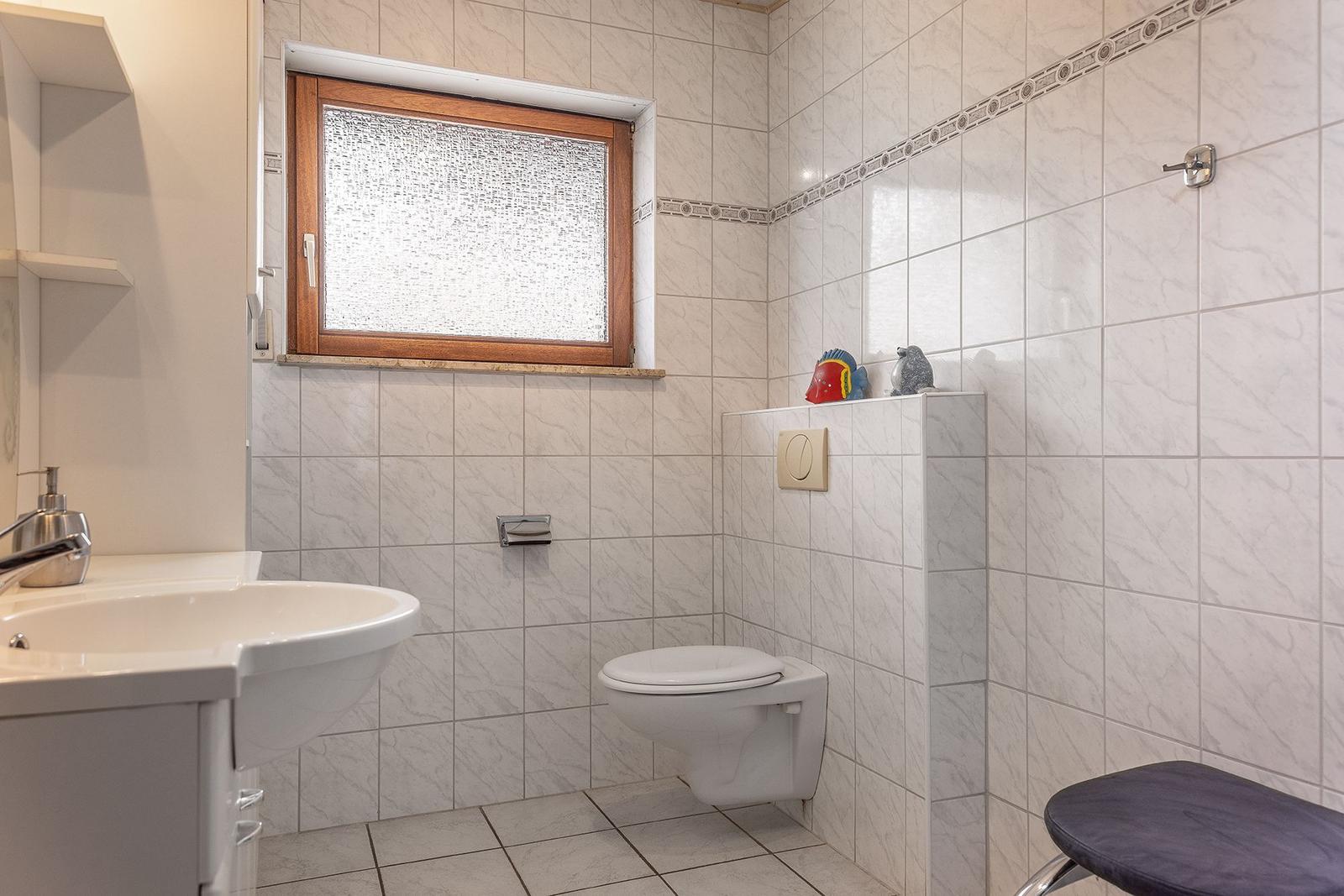 Badezimmer mit Toilette, Waschbecken und Fenster mit getöntem Glas.
