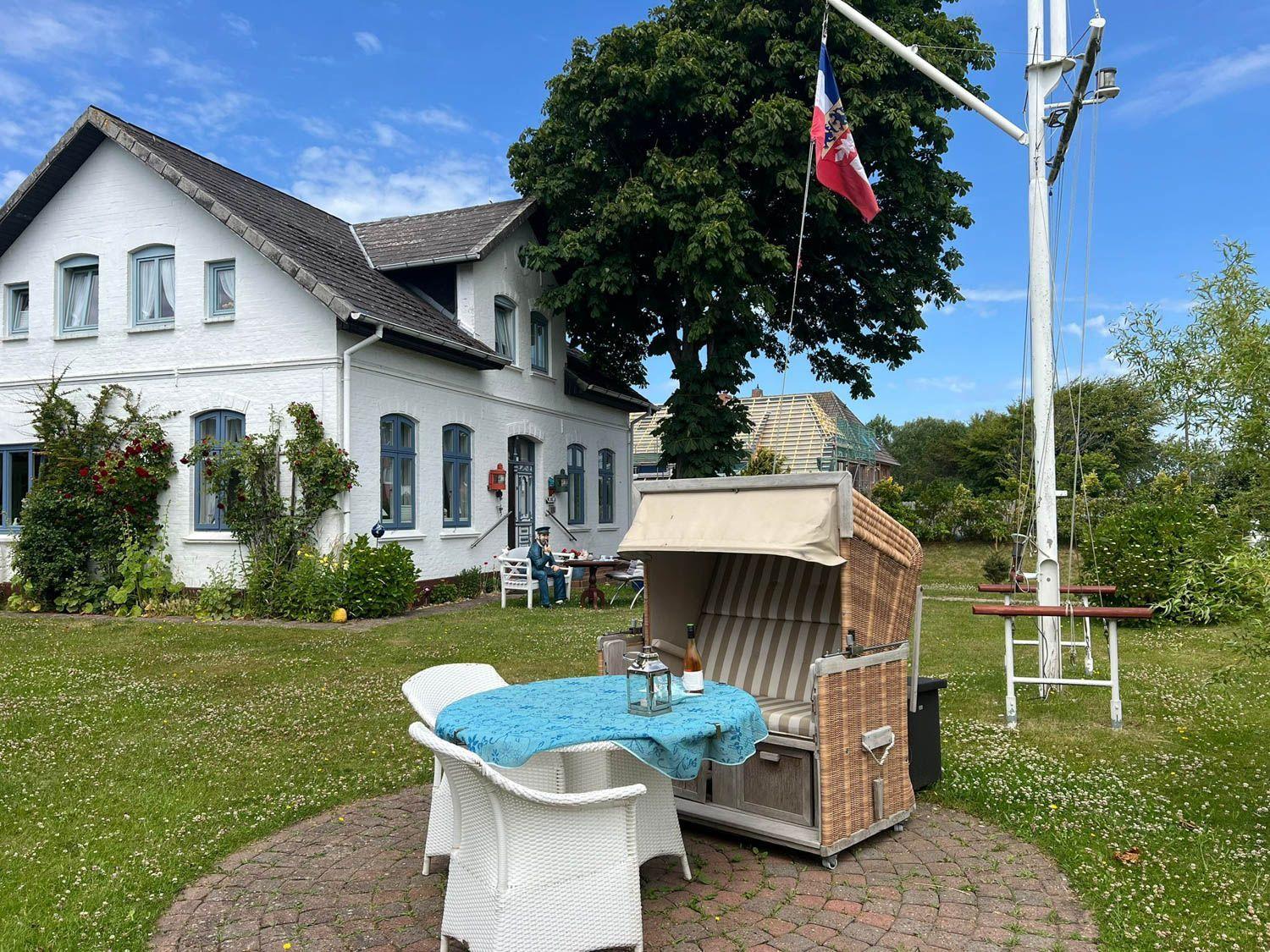 Wohnhaus mit Garten, Strandkorb und Tisch mit Stühlen. Flagge weht im Wind.