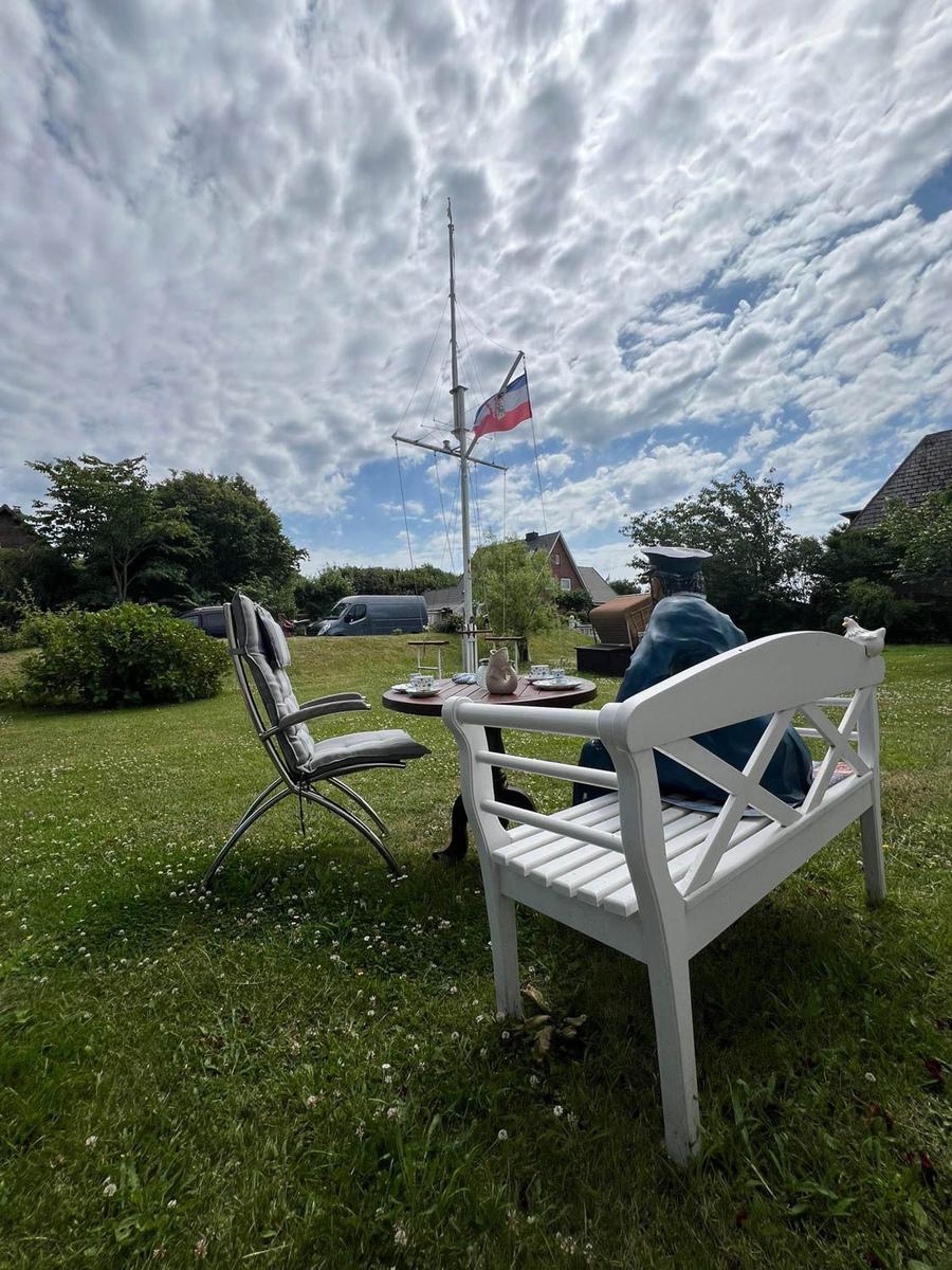 Garten mit Tisch, Stuhl und Segelboot auf Mast. Flagge weht im Wind.