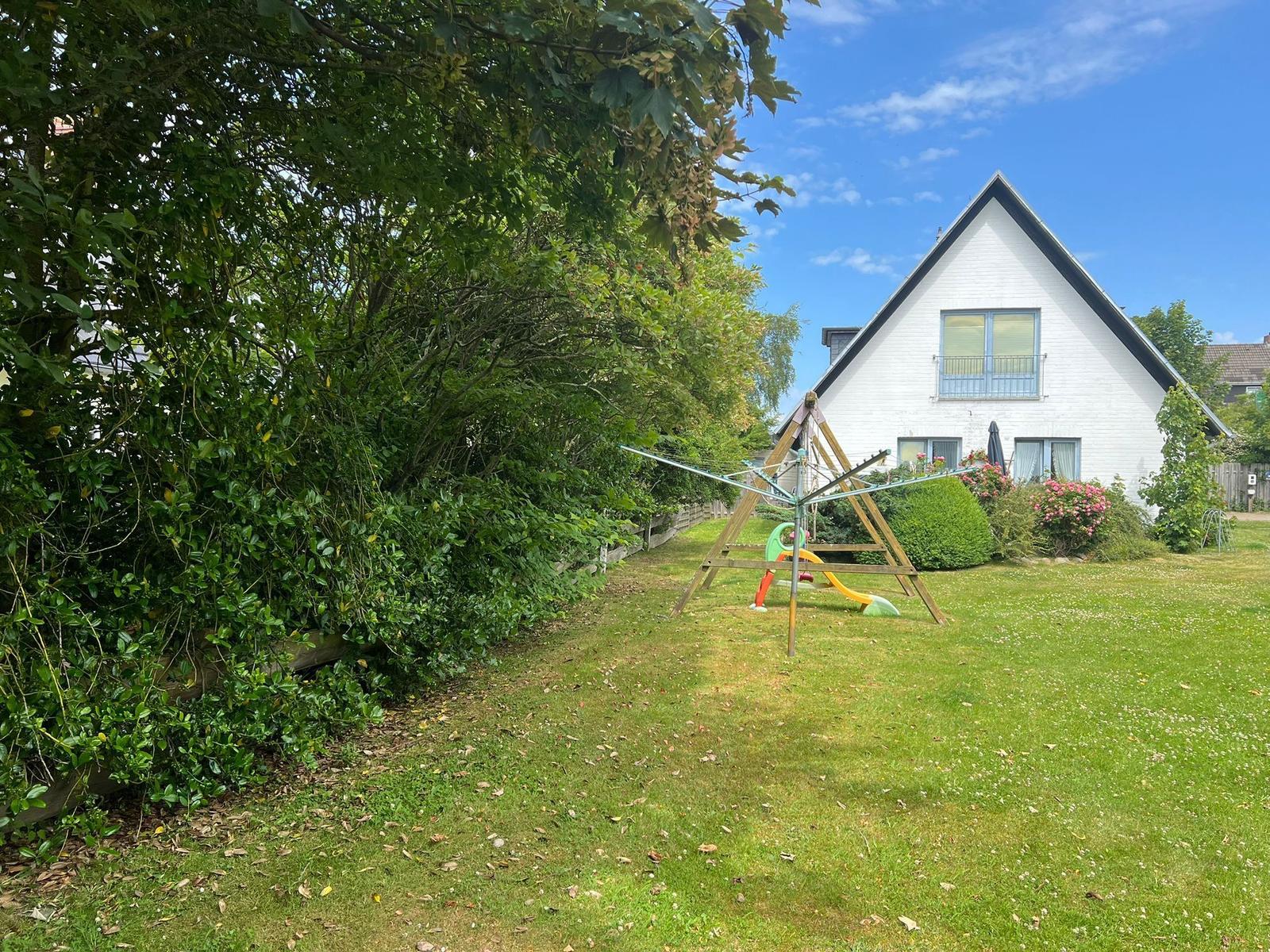 Ein weißes Haus mit Garten, Spielplatz und Blumen. Hinterhof mit Bäumen und einem Wäscheständer.