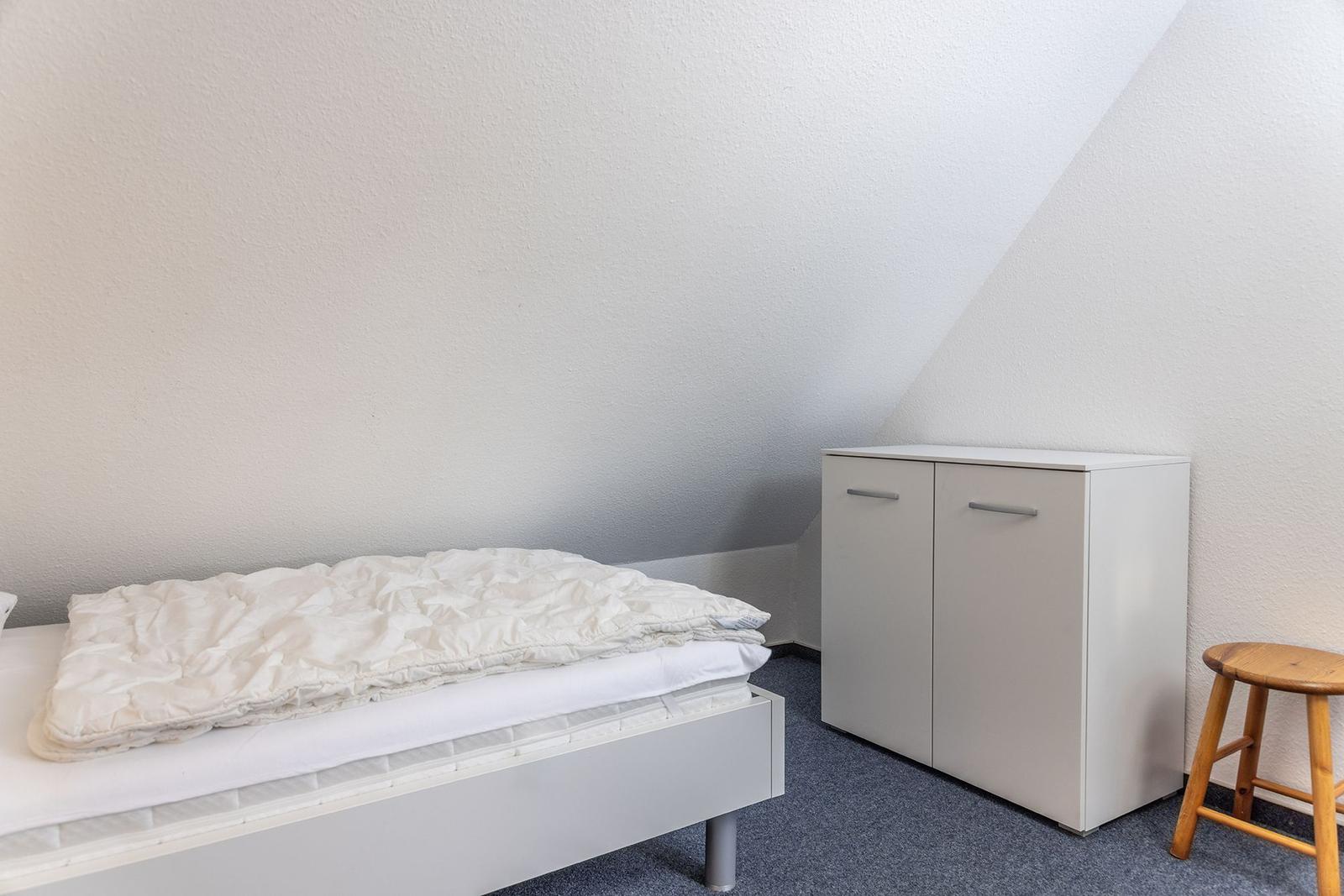Schlafzimmer mit Bett, Kleiderschrank und Hocker unter schrägem Dach