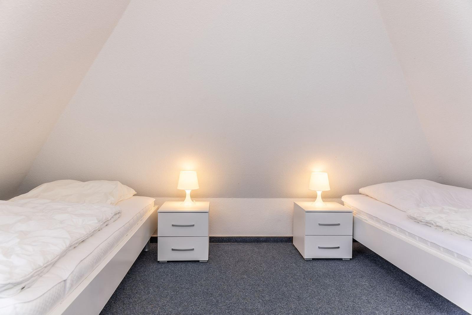 Zwei weiße Betten mit Nachttischen und Lampen unter schrägen Wänden.
