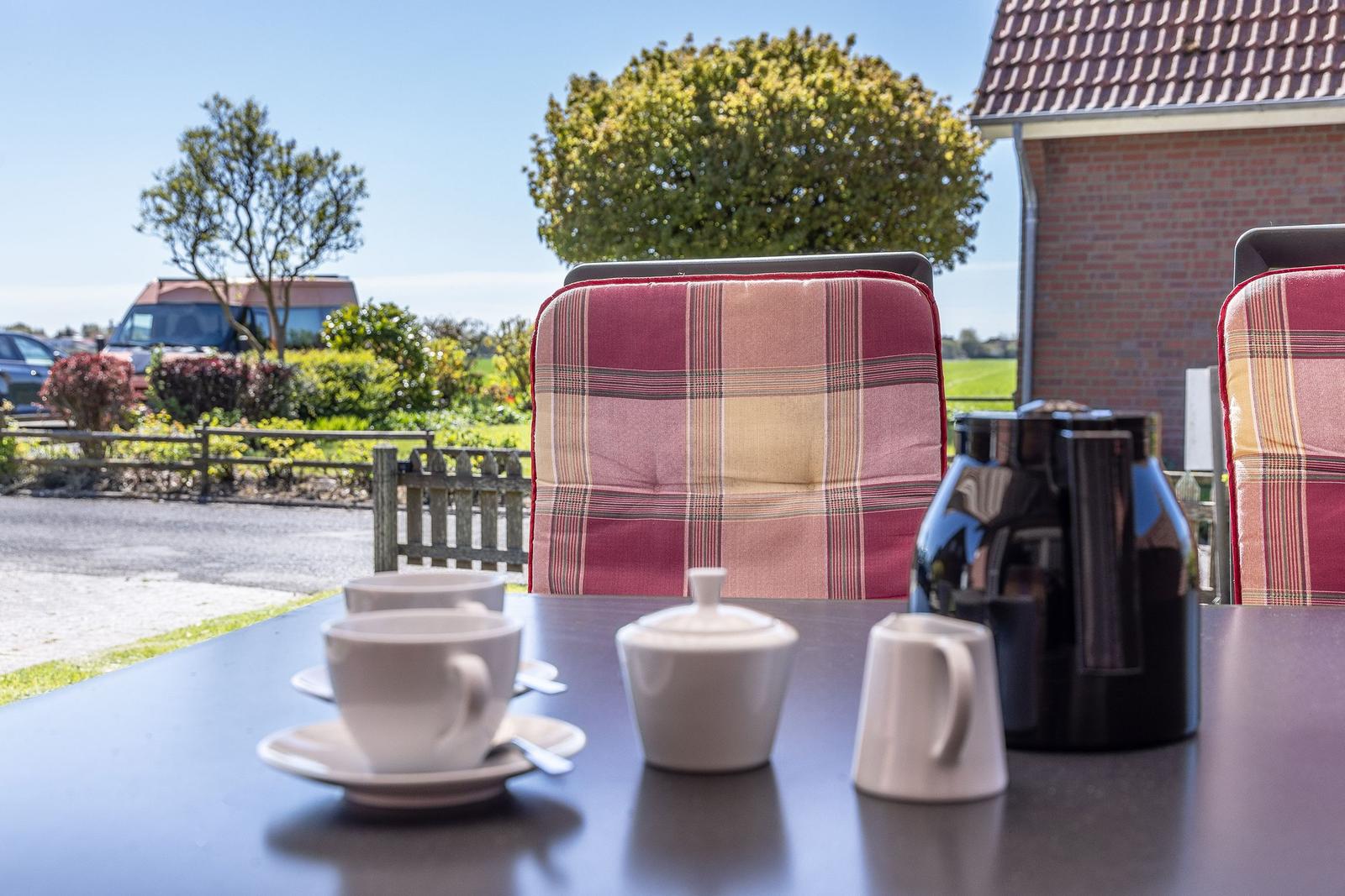 Tisch mit Tassen, Teekanne und Stühlen im Freien vor einem Haus