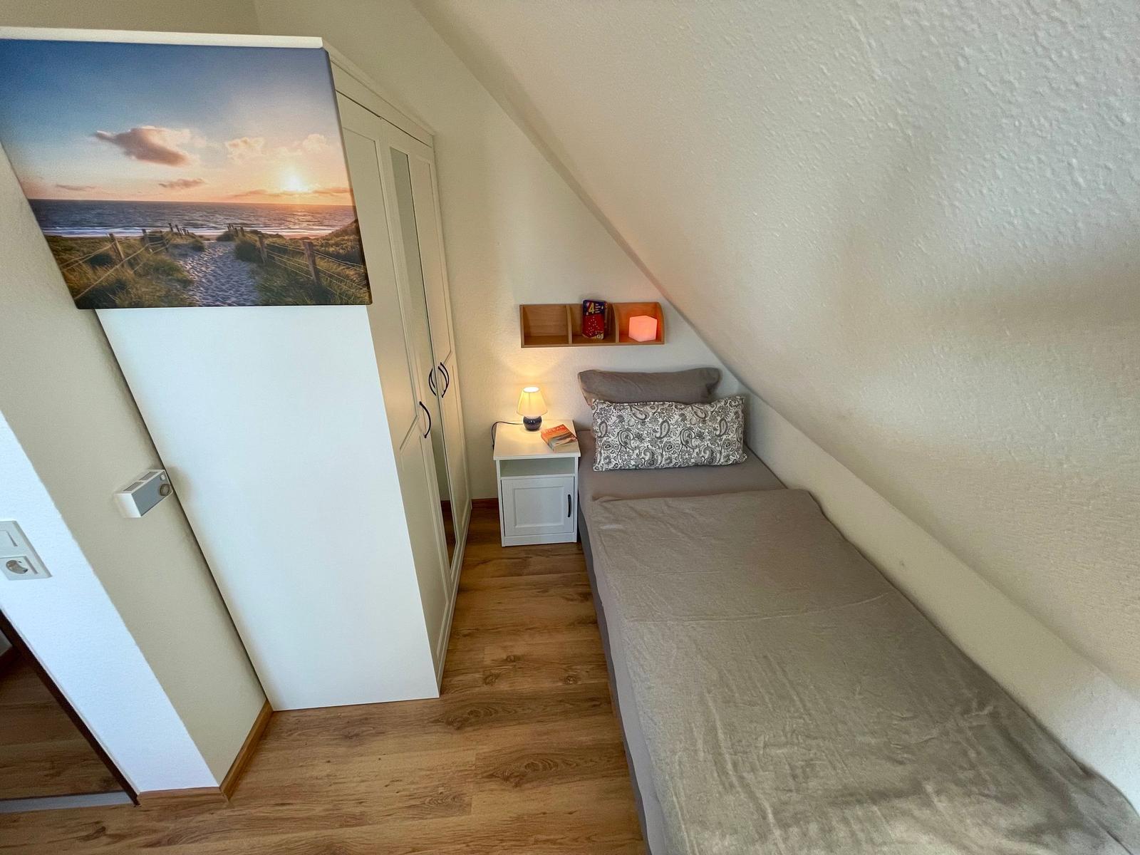 Ein Schlafzimmer mit Dachschräge, Bett, Nachttisch und Kleiderschrank.