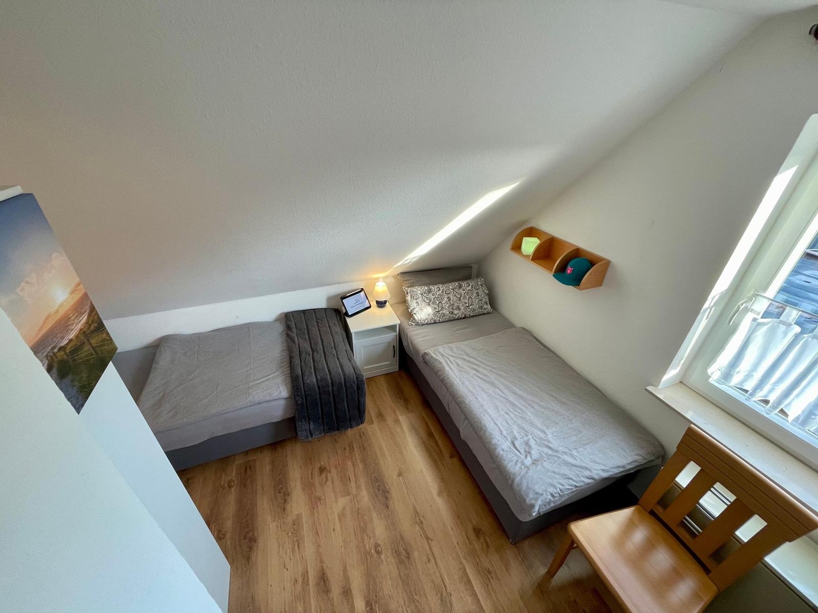 Zwei Einzelbetten, Nachttisch, Stuhl und Fenster im Dachzimmer.
