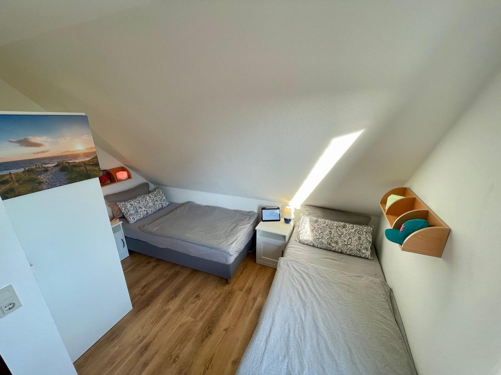 Zimmer mit zwei Betten, Holzboden und Dachschräge. Wandbild und Nachttisch sichtbar.