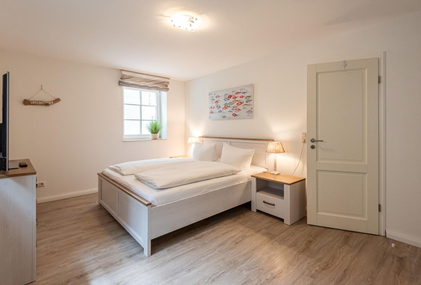 Schlafzimmer mit Bett, Nachttisch, Fenster und Tür.