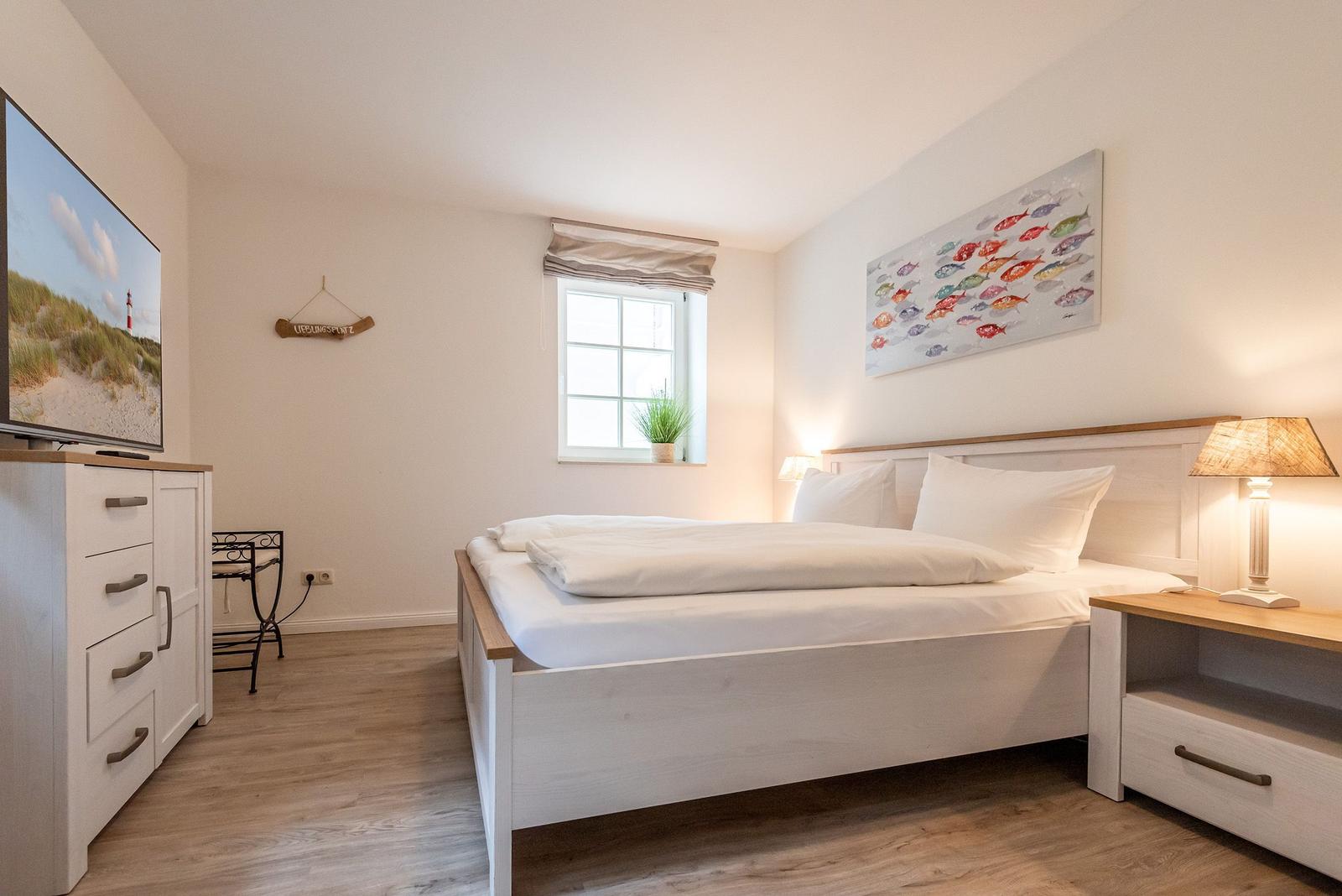 Schlafzimmer mit Bett, Nachttisch, Fernseher und Fenster.