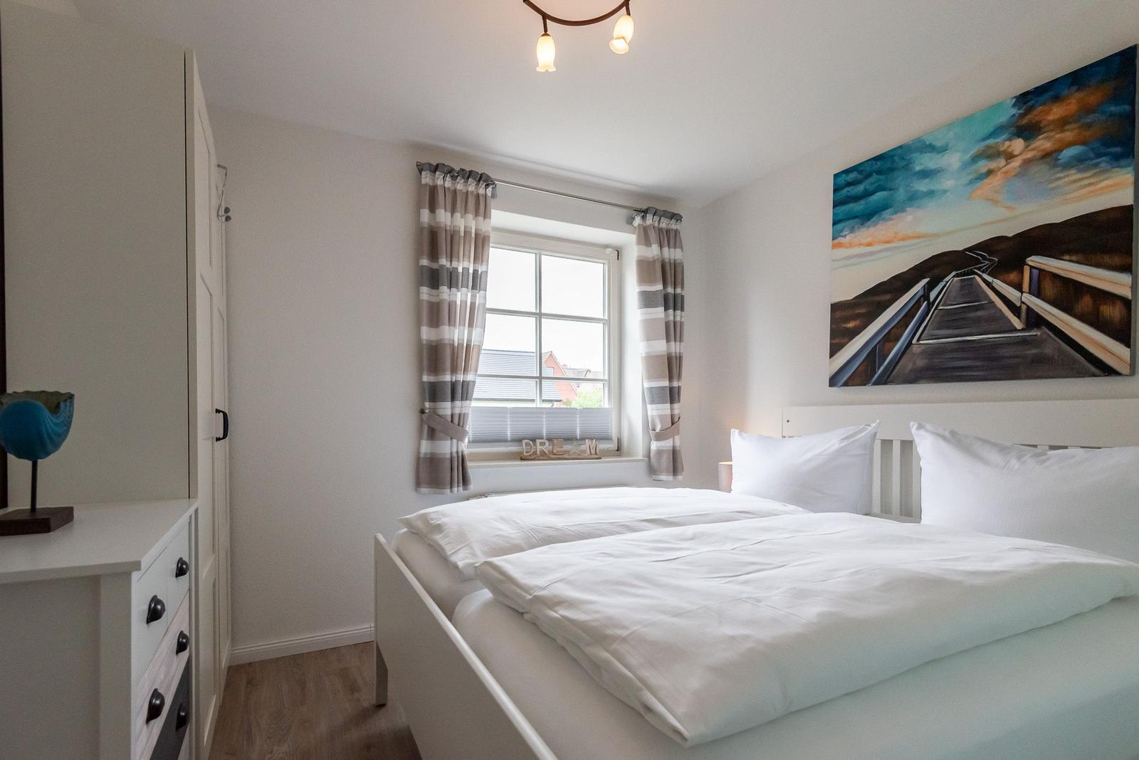 Schlafzimmer mit Doppelbett, Fenster mit Gardinen und Wandbild.