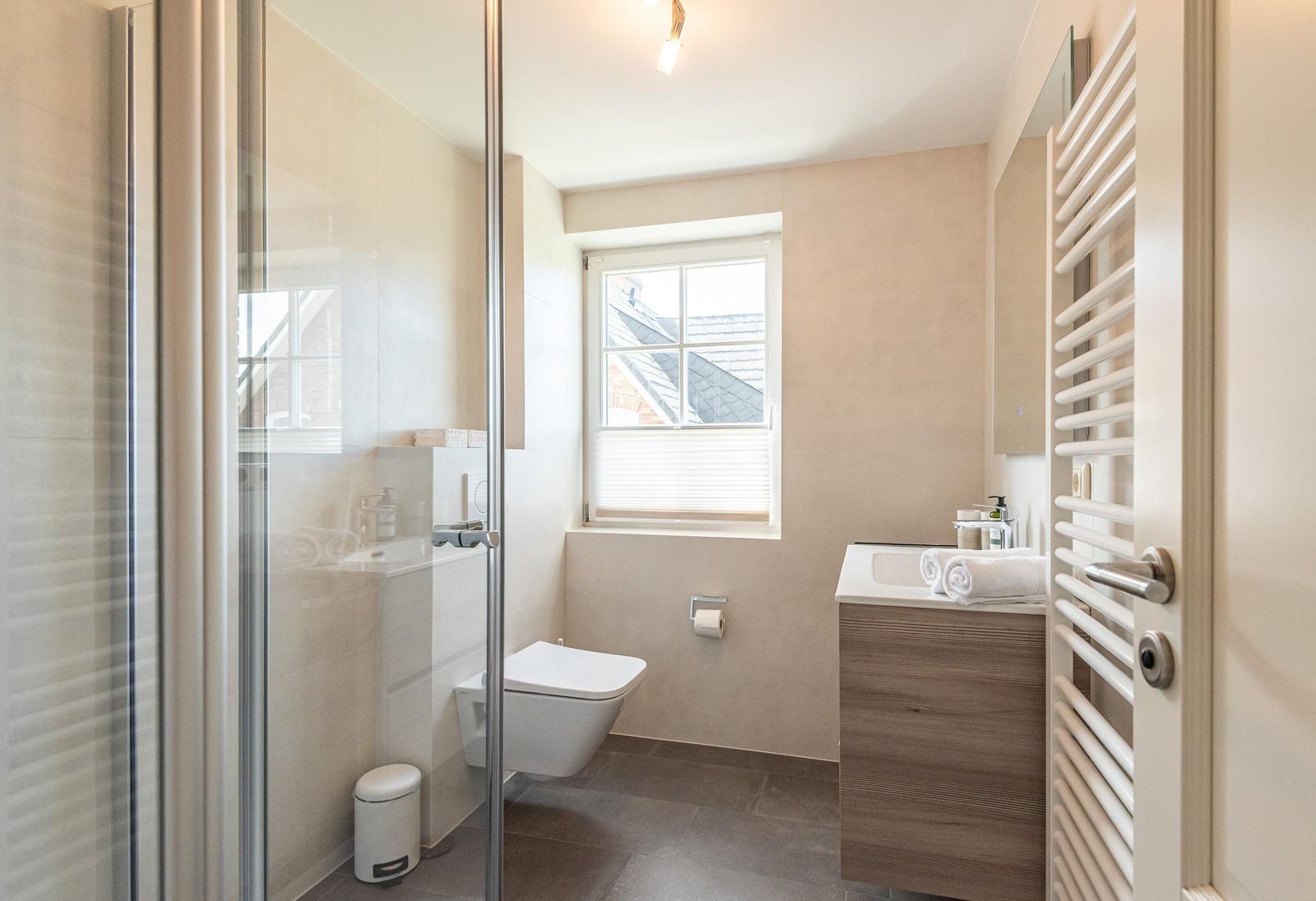 Badezimmer mit Dusche, Toilette, Waschbecken und Fenster