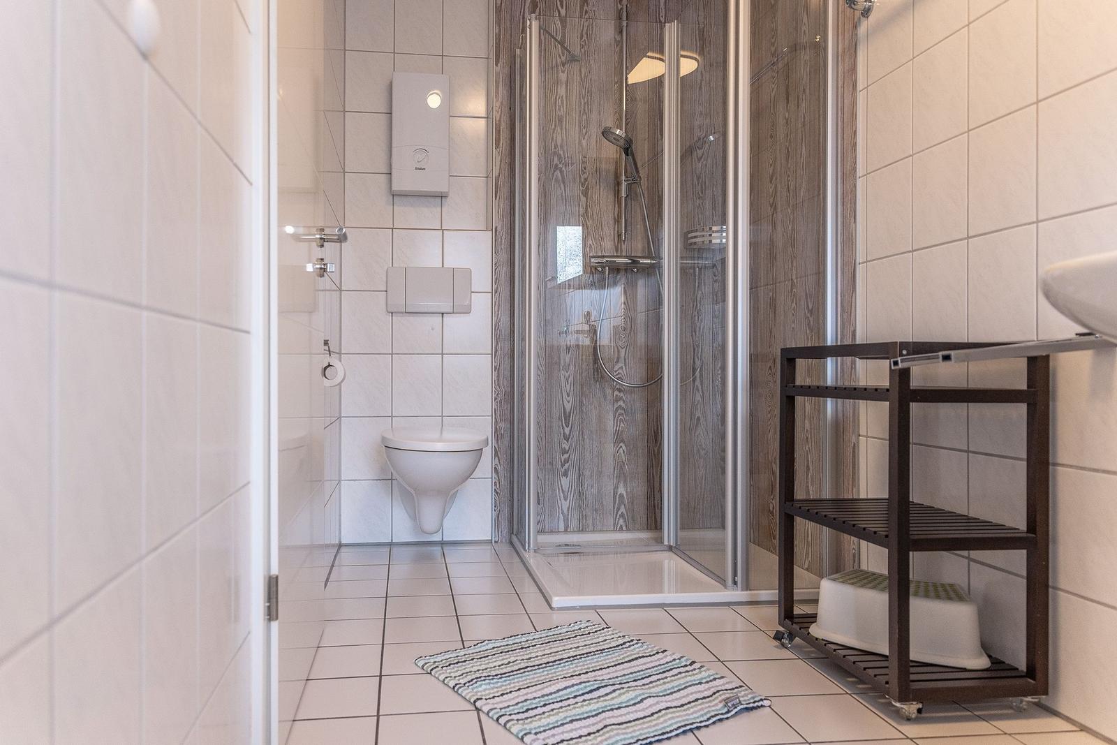 Badezimmer mit Dusche, Toilette und Waschbecken. Fliesenboden und Handtuchständer.