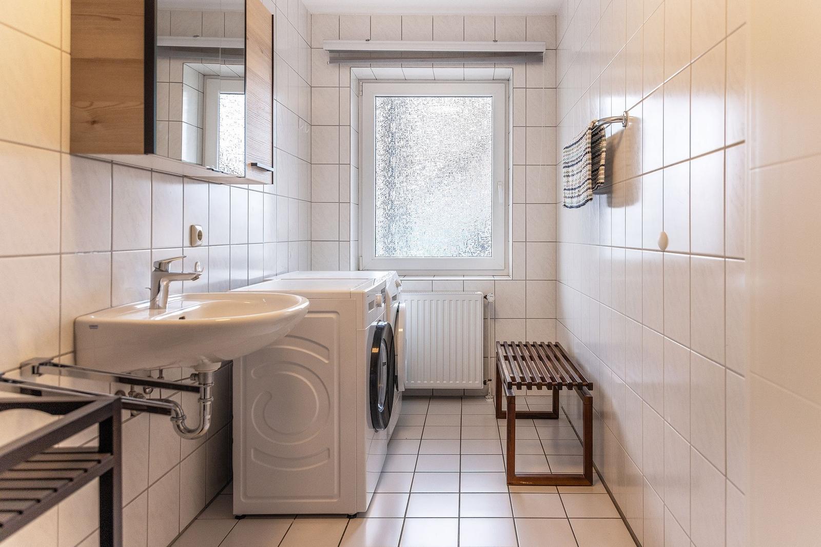 Badezimmer mit Waschmaschine, Spiegel und Fenster.