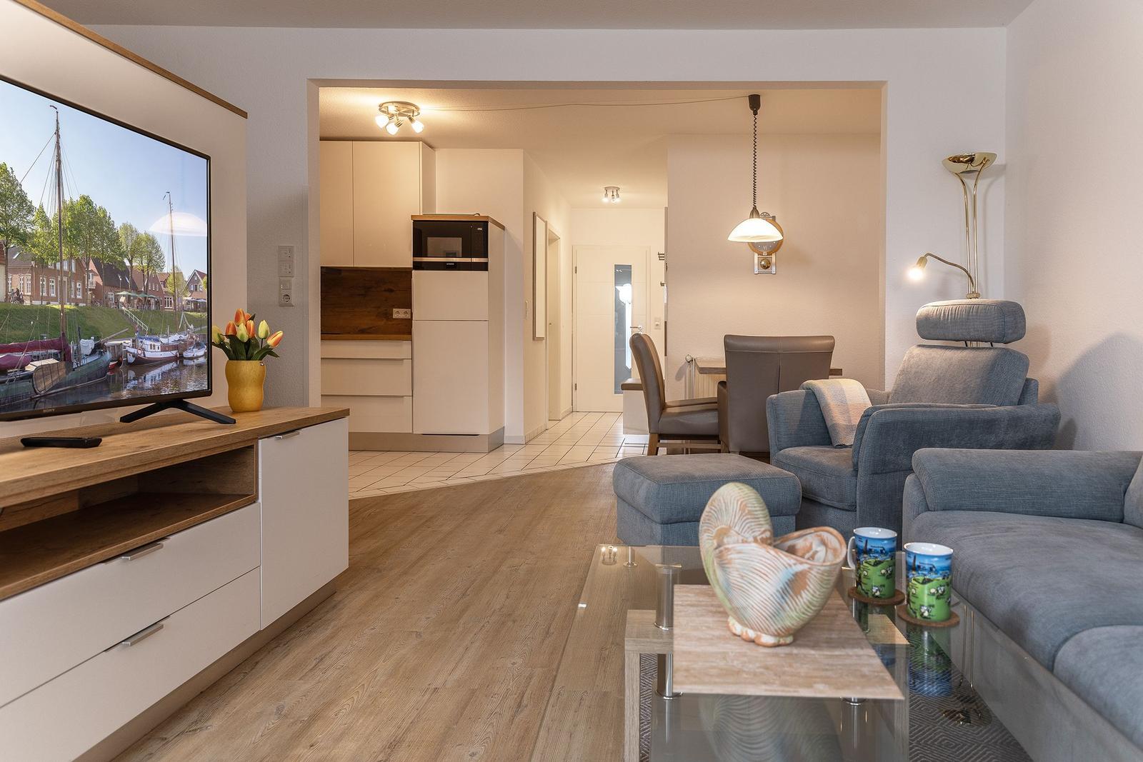 Wohnzimmer mit Sofa, Fernseher und Blick in die Küche