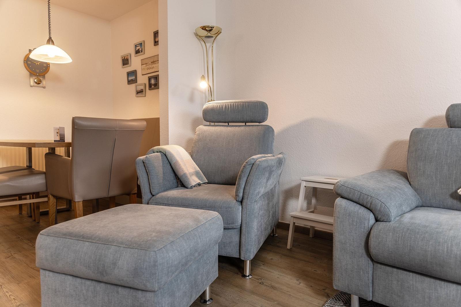 Wohnbereich mit grauen Sesseln, Beistelltisch und Stehlampe. Hintergrund zeigt Essbereich mit Tisch und Stühlen.
