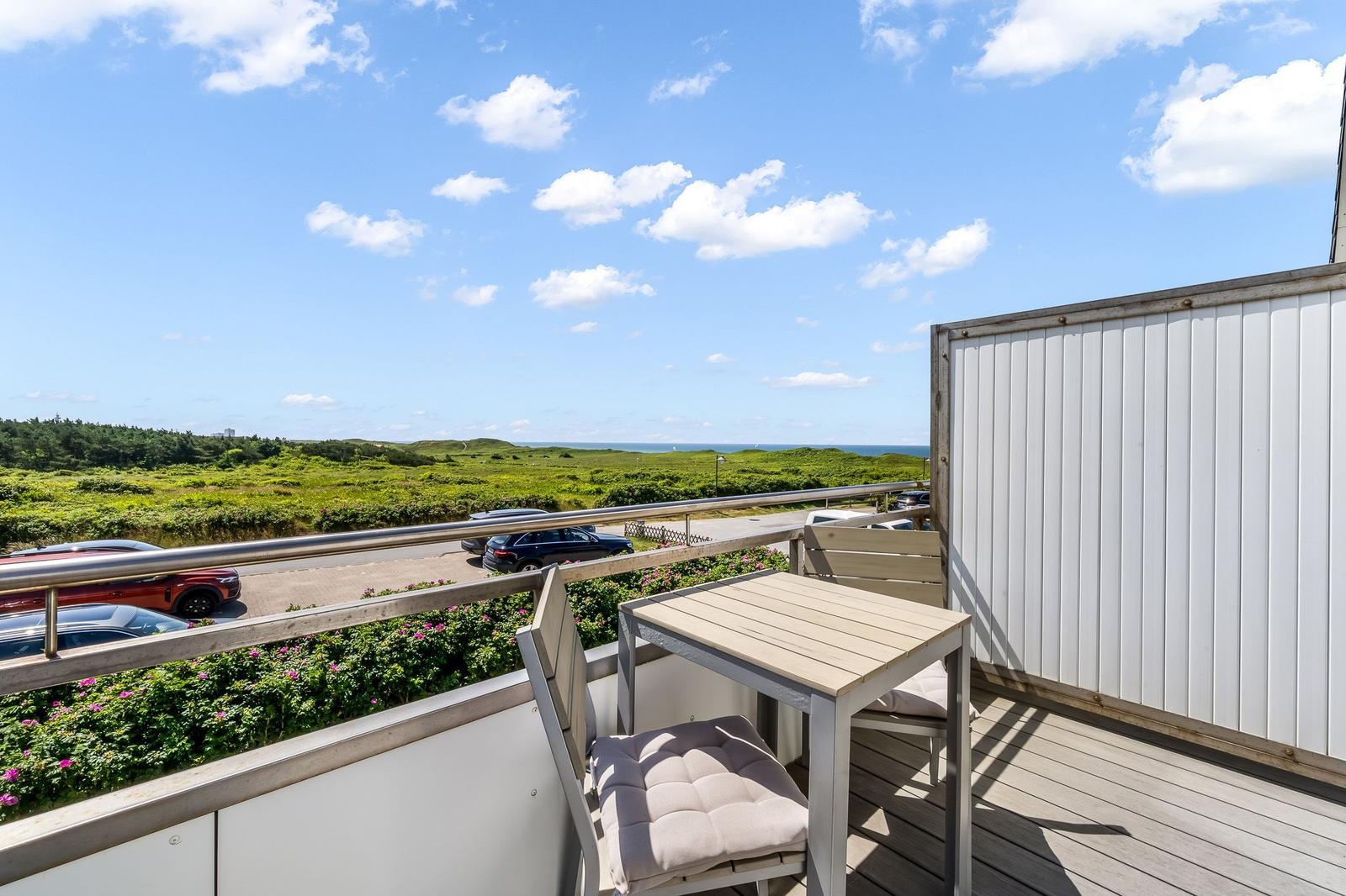 Terrasse mit Tisch und Stühlen, Blick auf grüne Landschaft und Meer.