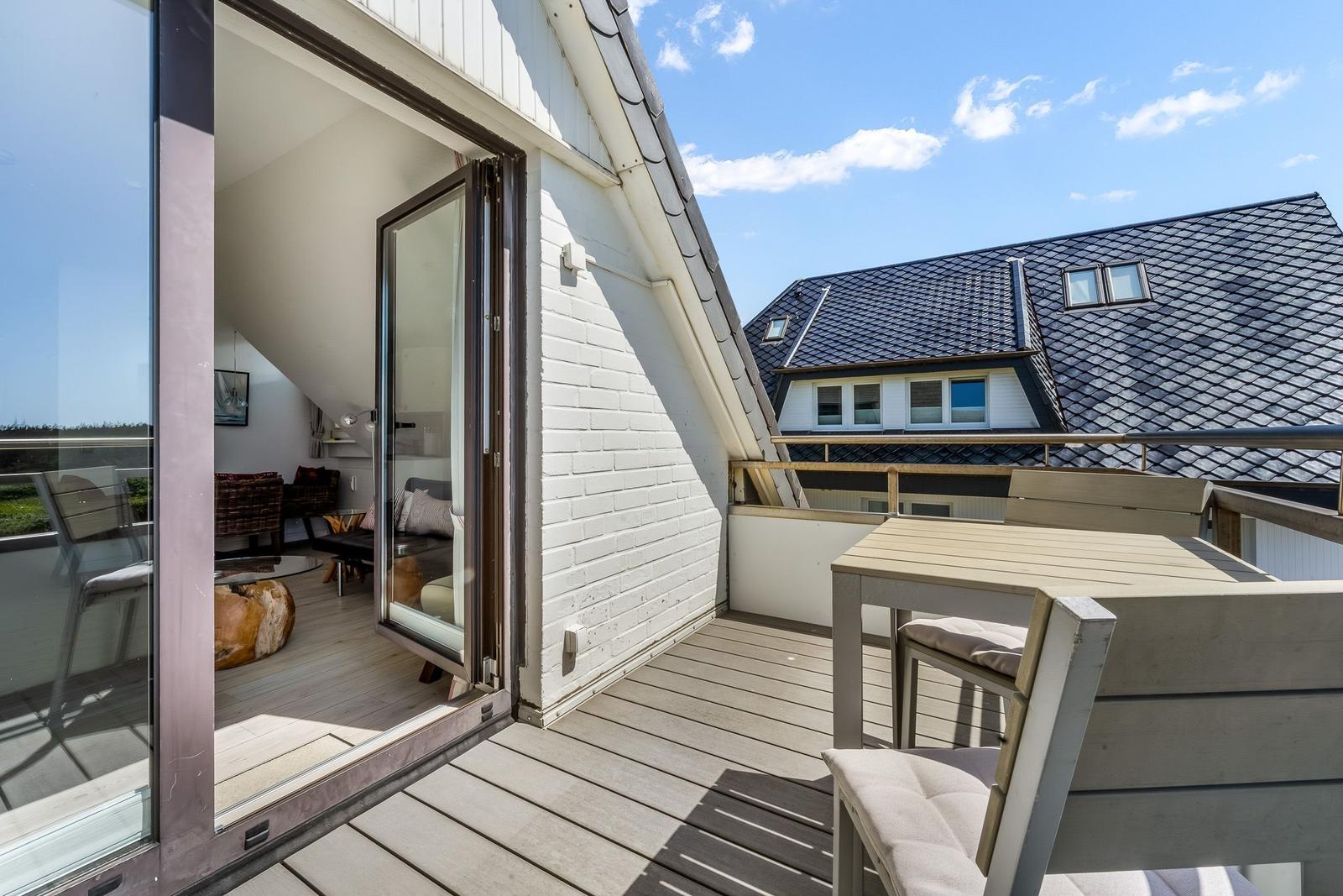 Terrasse mit Tisch und Stühlen, Blick auf Haus mit Schieferdach und Innenraum über Glas-Tür.