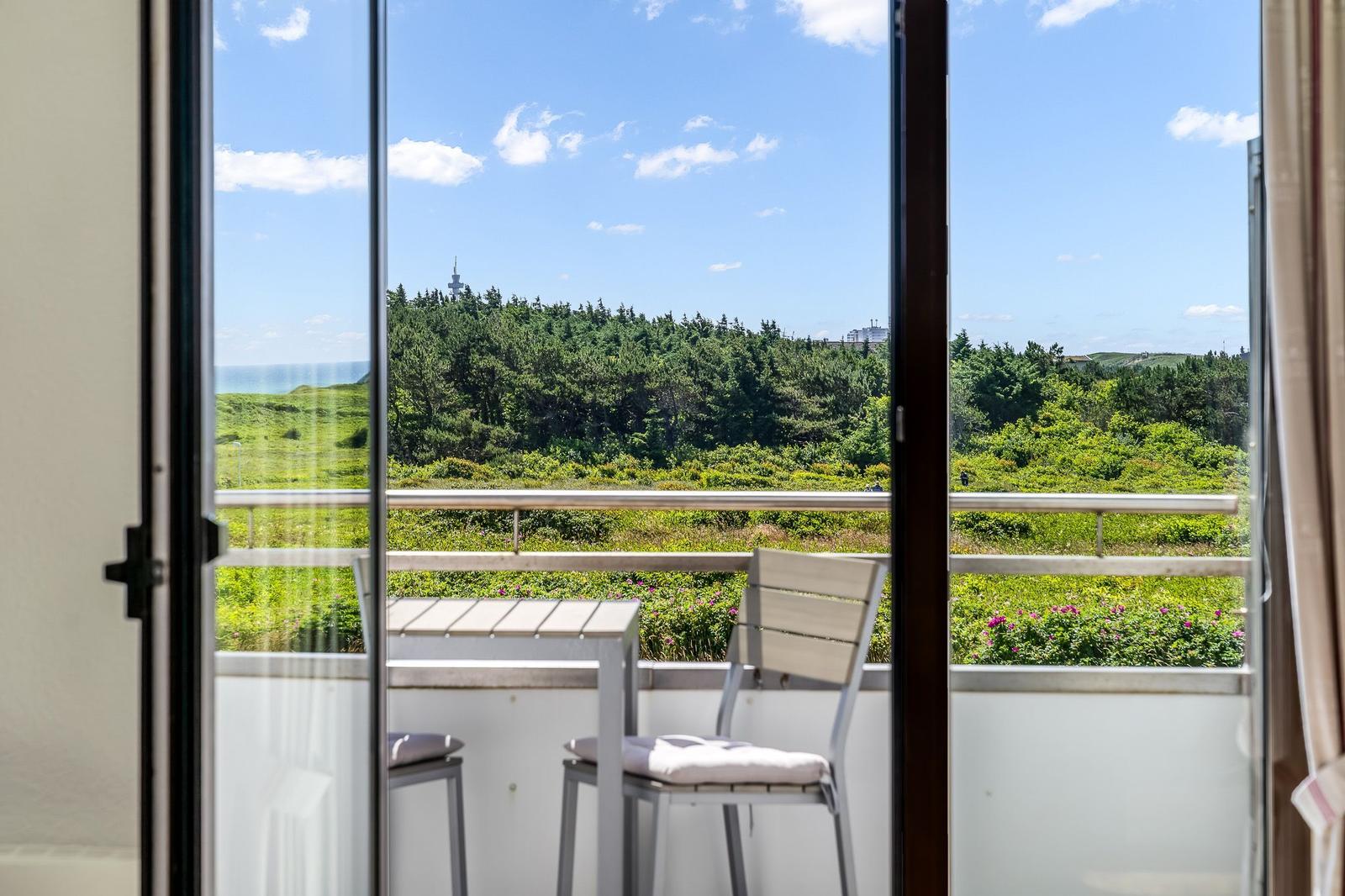 Balkon mit Tisch und Stühlen bietet Blick auf grüne Landschaft und Meer.