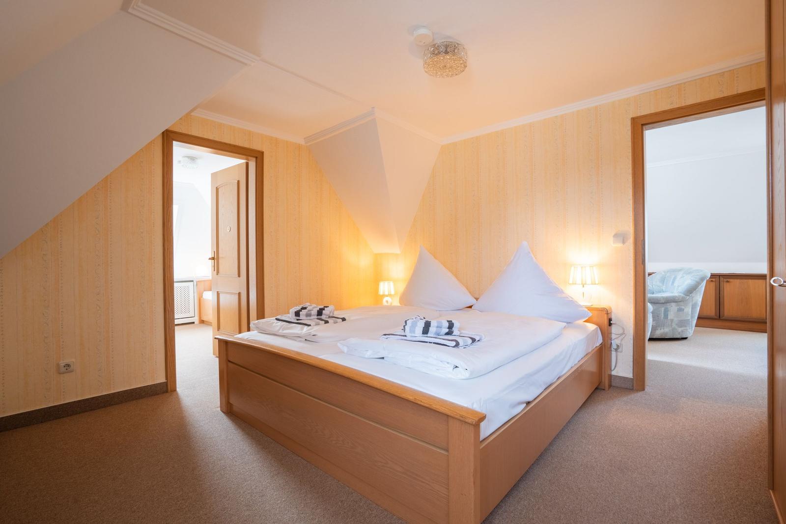 Schlafzimmer mit Holzbett, Beleuchtung und Tür zu angrenzenden Räumen.