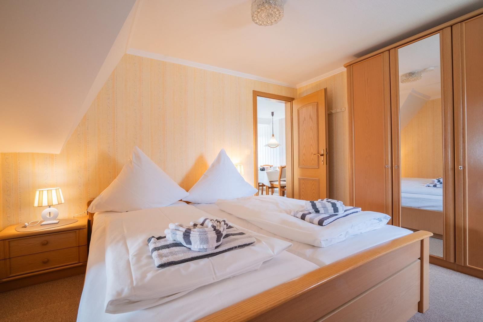 Schlafzimmer mit Doppelbett, Holzmöbeln und Spiegelschrank. Blick in angrenzenden Raum.