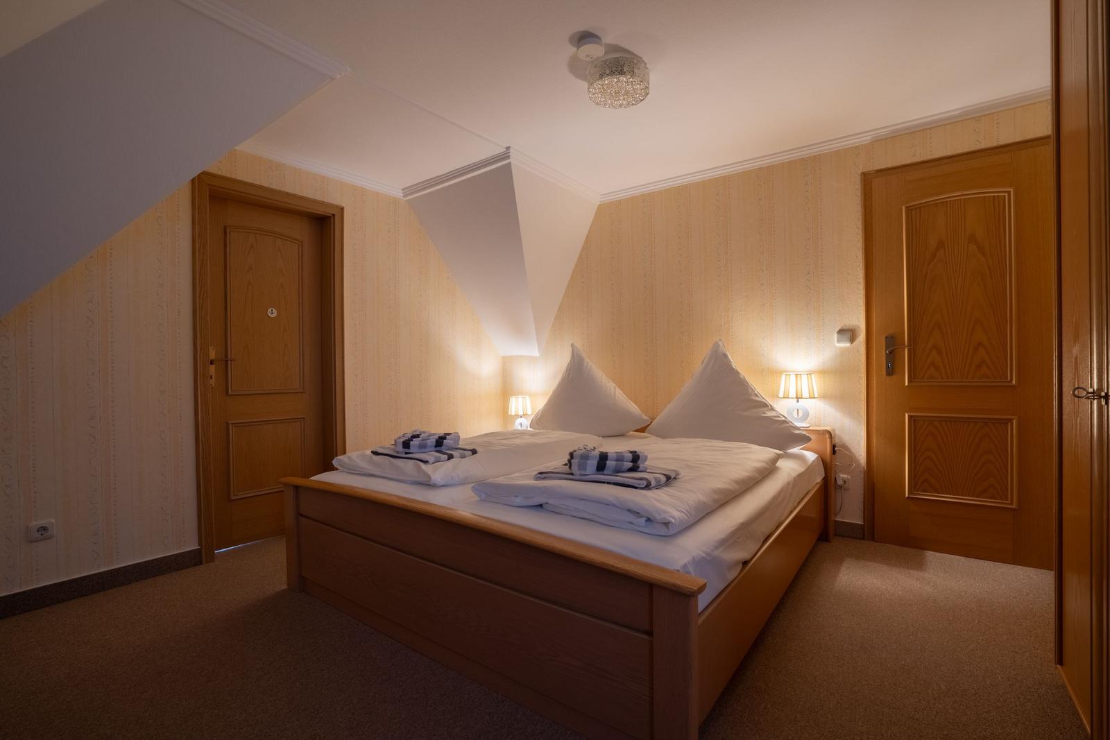 Schlafzimmer mit Doppelbett, Holztüren und Wandbeleuchtung.