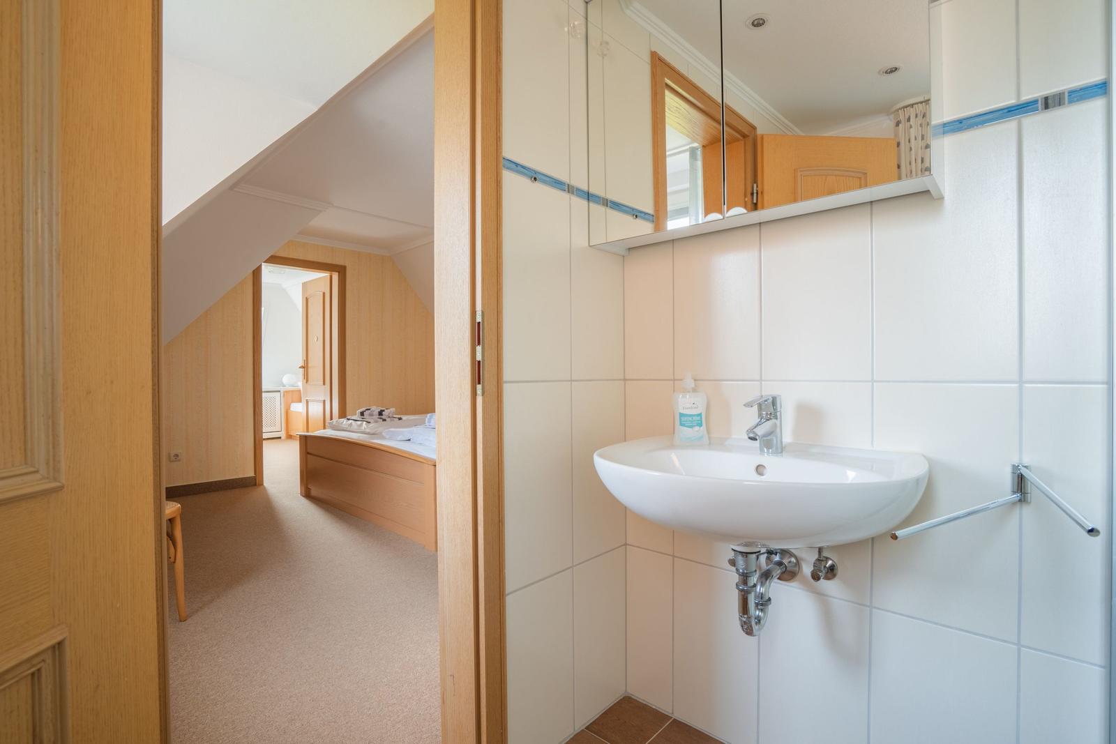 Badezimmer mit Waschbecken und Spiegel. Blick in das Schlafzimmer mit Bett.