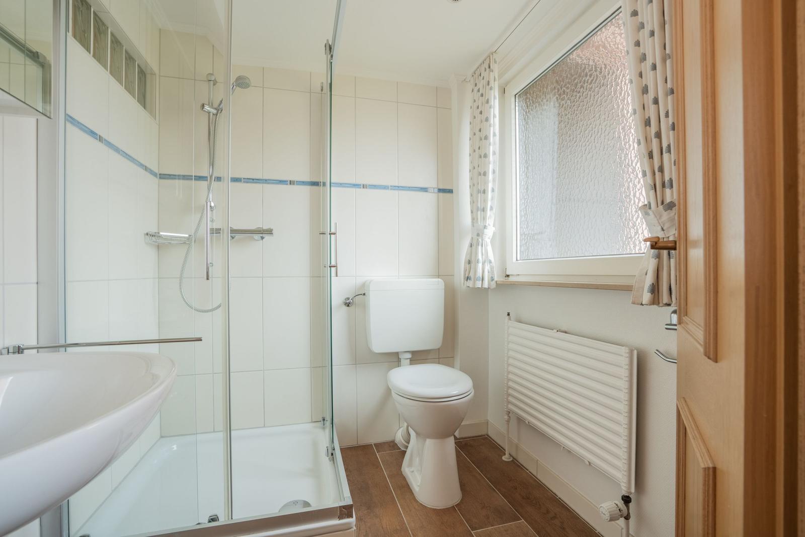 Badezimmer mit Dusche, Toilette und Fenster mit Vorhängen.