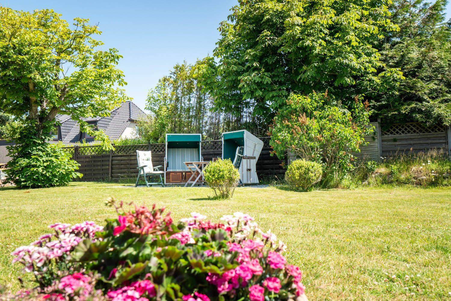 Garten mit zwei Liegestühlen und Blumenbeet im Vordergrund.