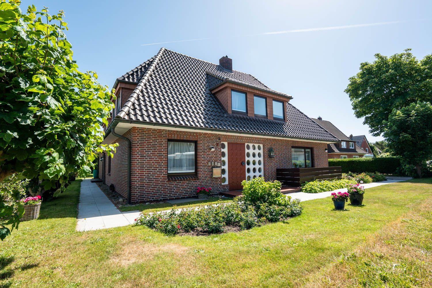 Ein Haus mit Ziegelfassade, Dachgauben und Garten mit Blumen.