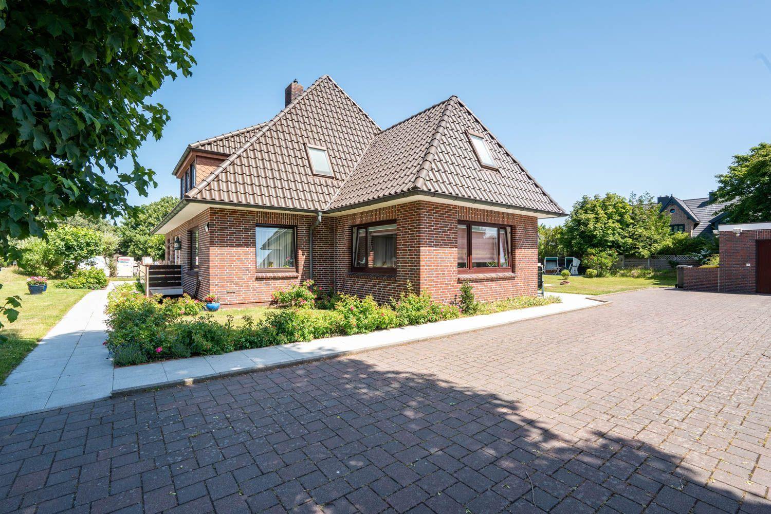 Ein zweistöckiges Haus mit Ziegelfassade und Dachgauben. Vor dem Haus befindet sich ein gepflasterter Hof.