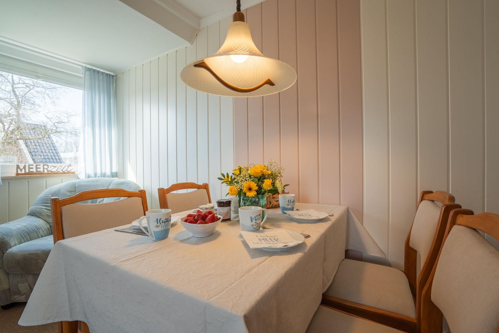 Esszimmer mit Tisch, Stühlen und Fensterblick. Deckenleuchte und Blumenarrangement.