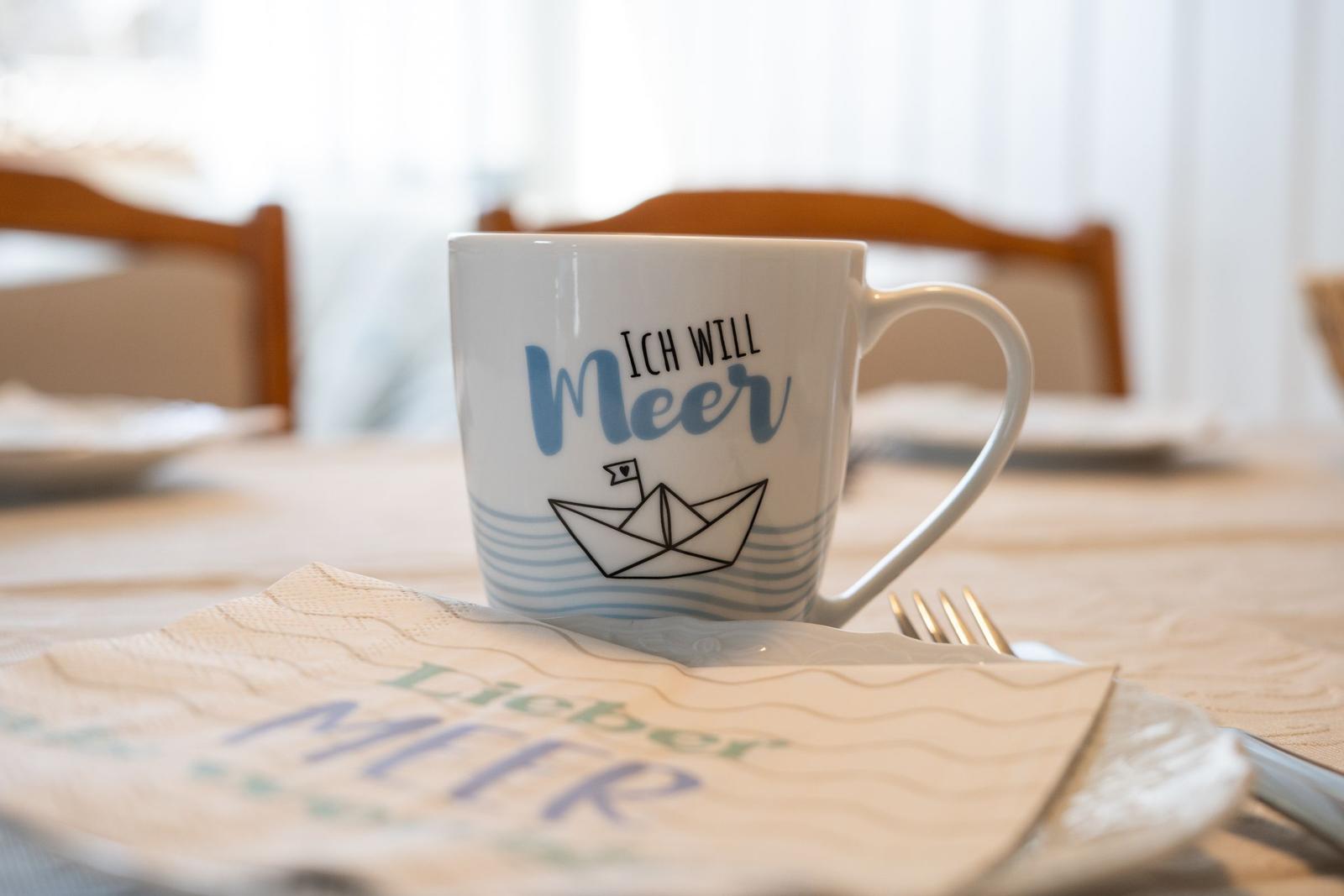 Eine Tasse mit Meer-Motiv steht auf einem Tischtuch mit Wellenmuster.