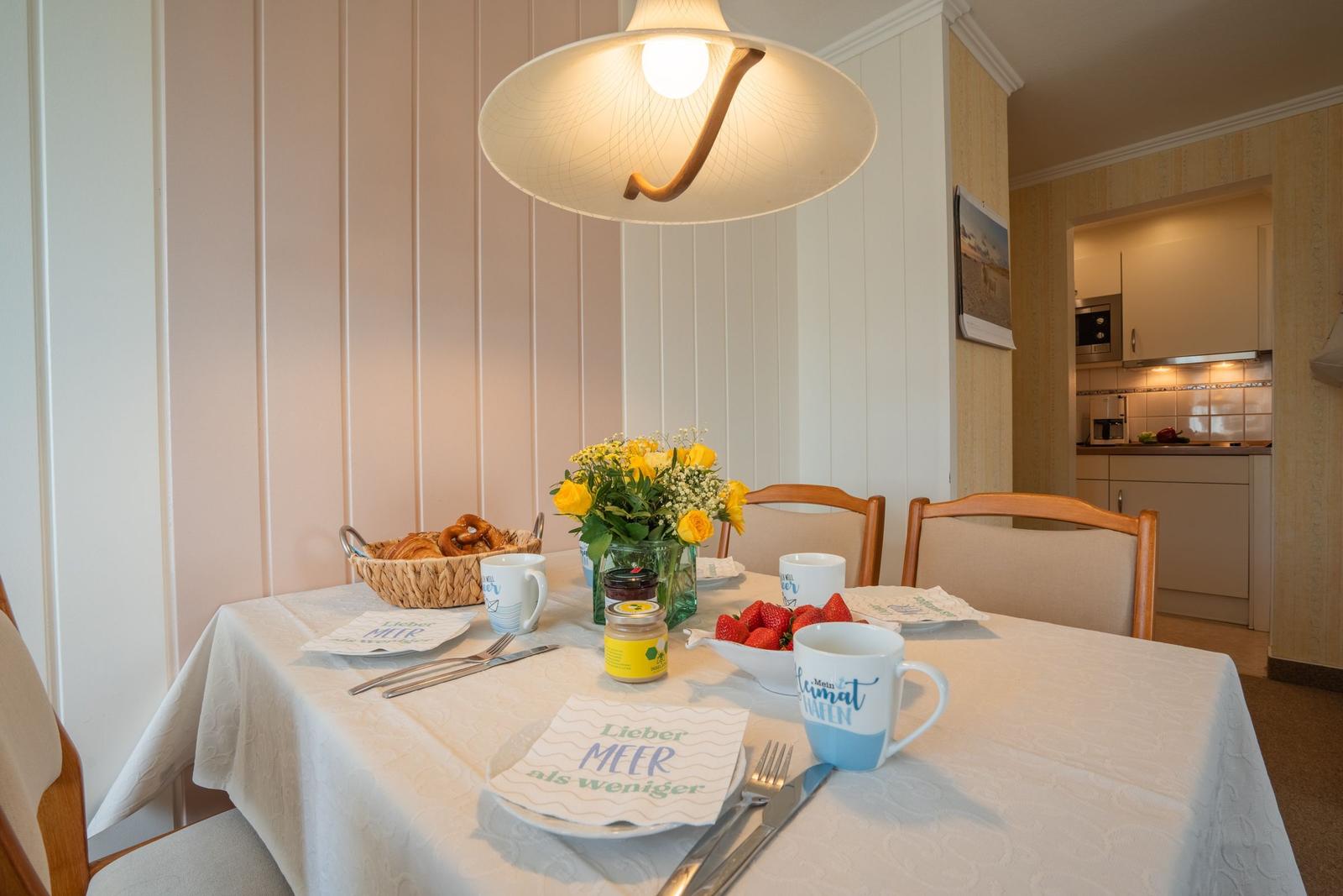 Gedeckter Tisch mit Frühstück, Blumen und Kaffeetassen in einem Wohnraum.