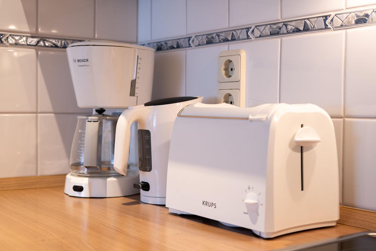 Küchenzeile mit Kaffeemaschine, Wasserkocher und Toaster auf Holzoberfläche.