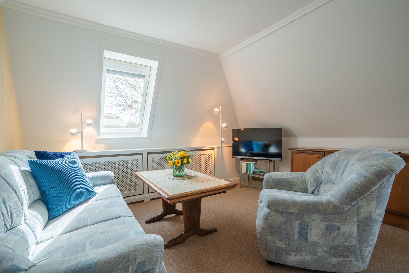 Wohnzimmer mit Sofa, Sessel, Couchtisch und Fernseher unter Dachschräge.