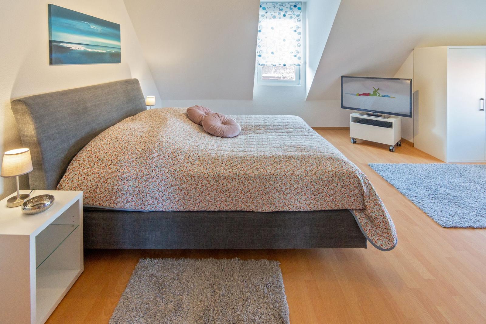 Schlafzimmer mit Doppelbett, Fernseher und Fenster mit Vorhang.