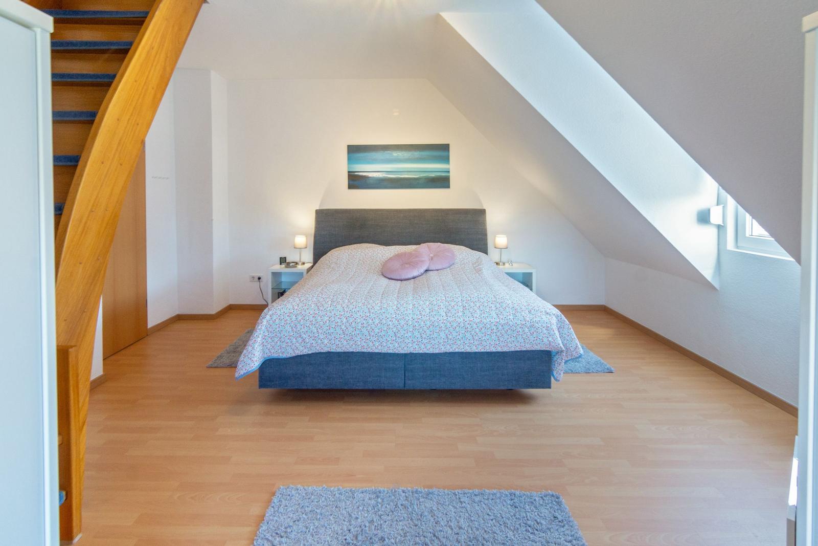 Schlafzimmer mit Dachschrägen, Bett, Nachttische und Wandbild.