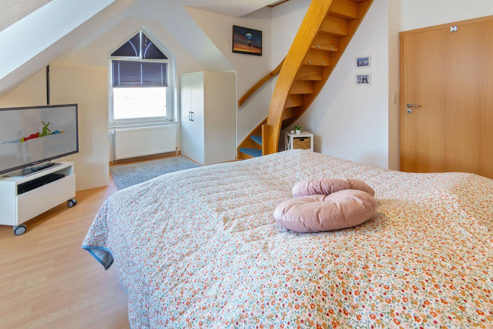 Schlafzimmer mit Doppelbett, Fernseher und Holztreppe.