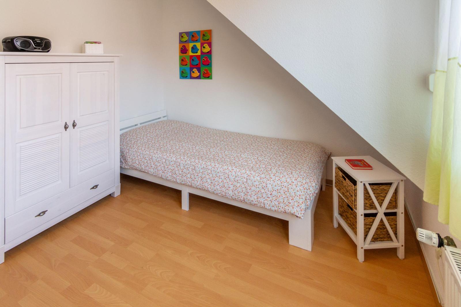 Schlafzimmer mit Einzelbett, weißen Schränken und Holzboden unter Dachschräge.