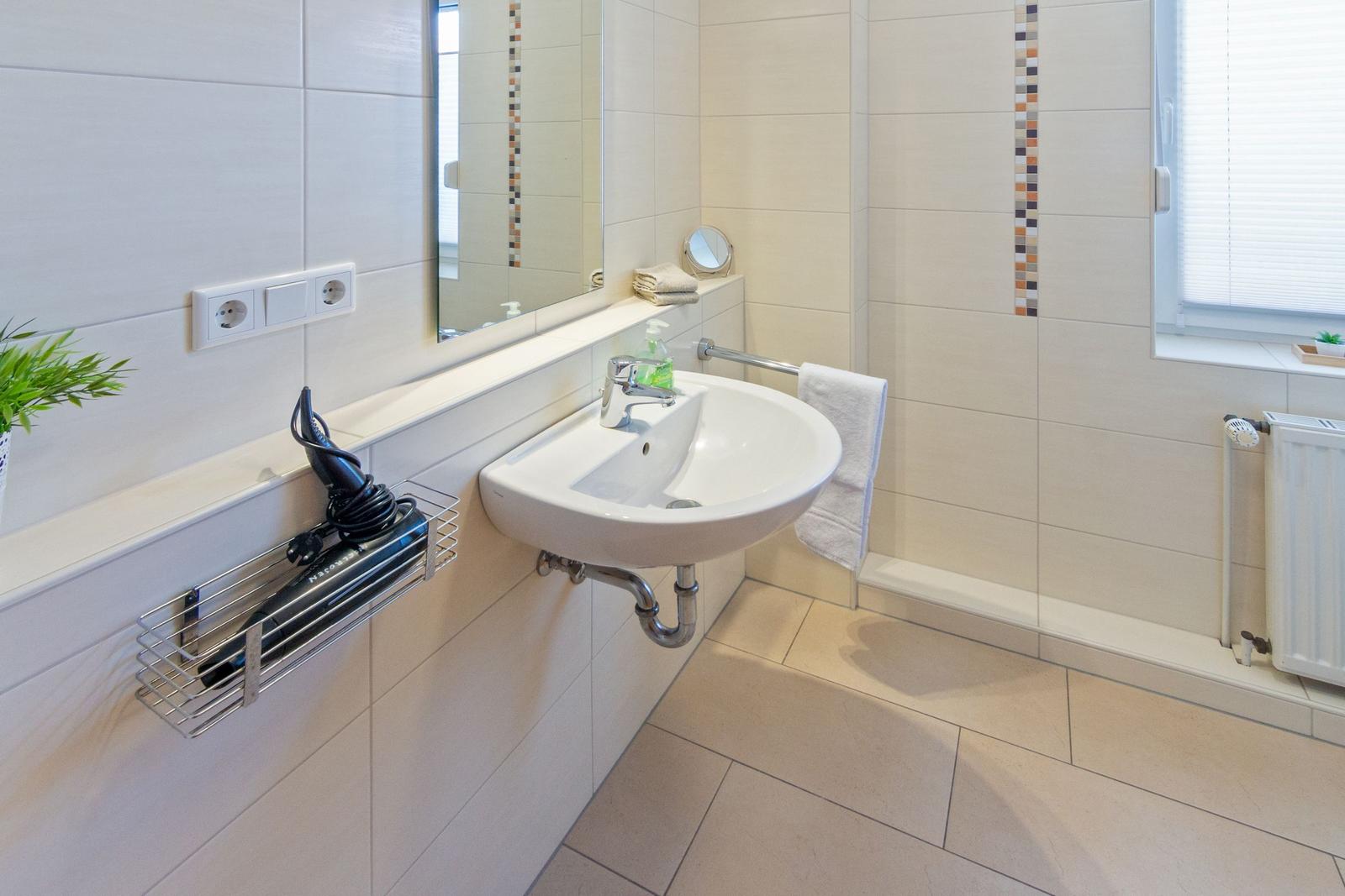 Badezimmer mit Waschbecken, Spiegel, Handtuch und Haartrockner.