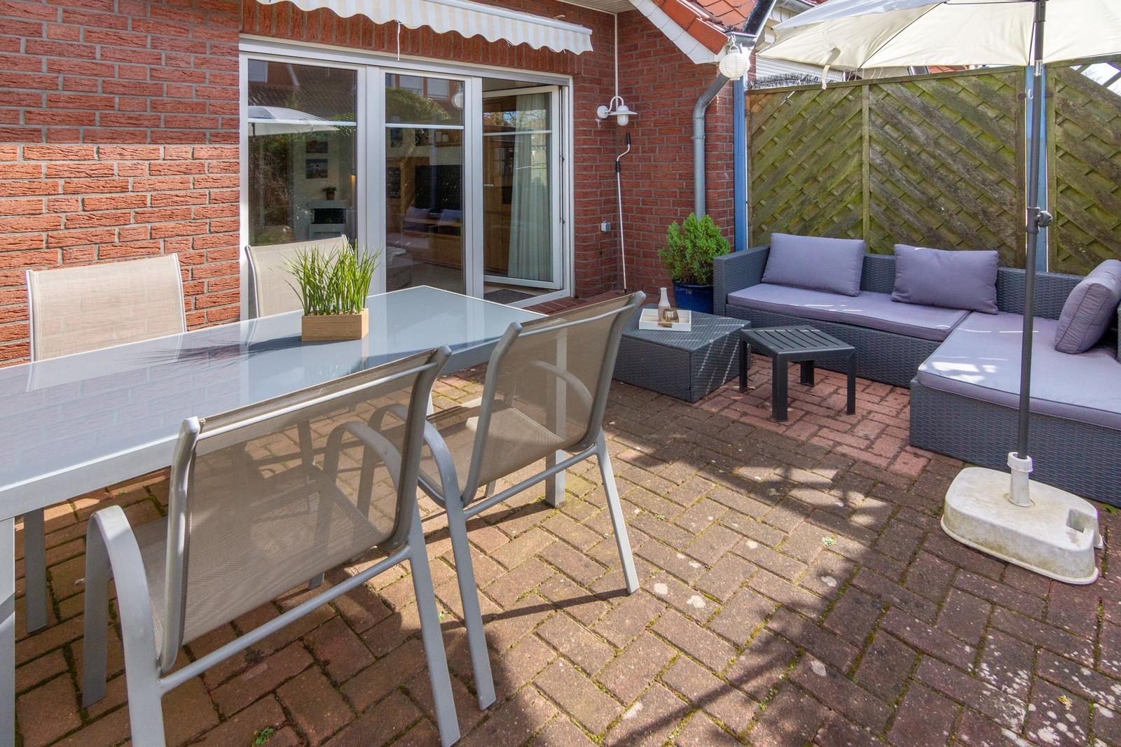 Terrasse mit Sitzgruppe, Tisch und Stühlen. Hinterhof mit Holzzaun und Glasfront.