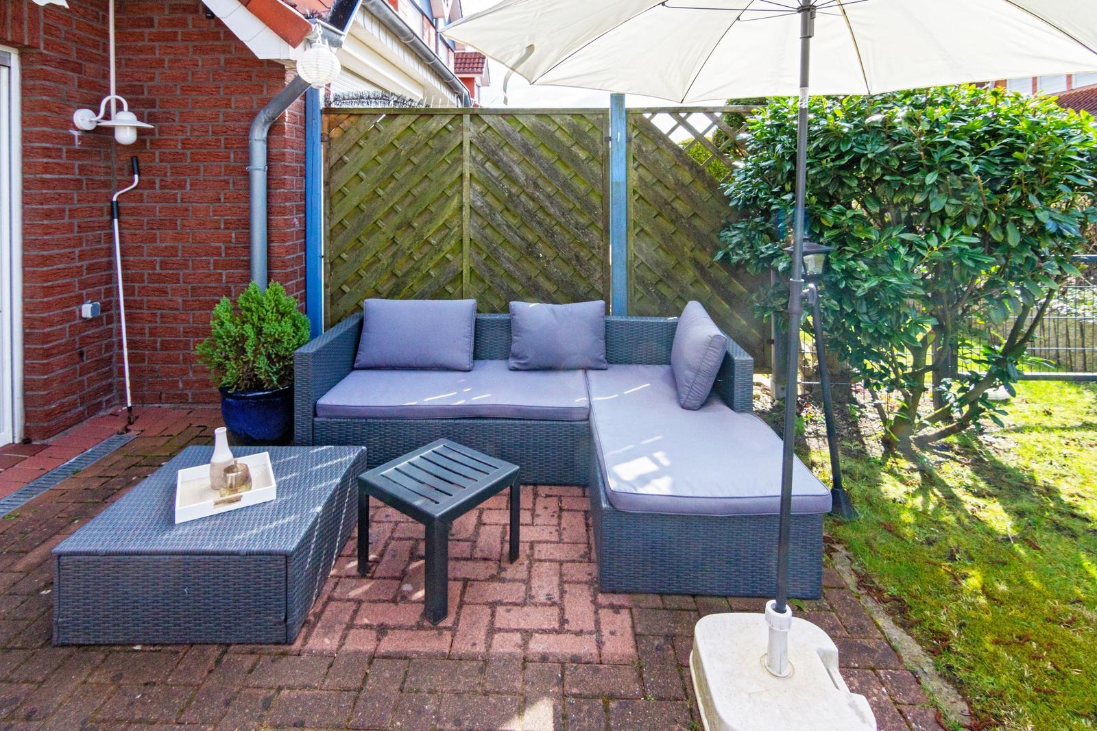 Terrasse mit Sitzgruppe, Sonnenschirm und Pflanzen. Holzgeländer und Ziegelsteinboden.