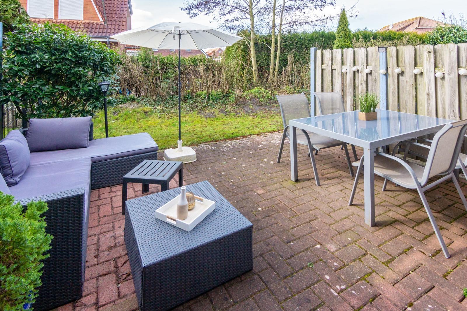 Terrasse mit Sitzgruppe, Tisch und Stühlen sowie Sonnenschirm auf gepflastertem Boden.