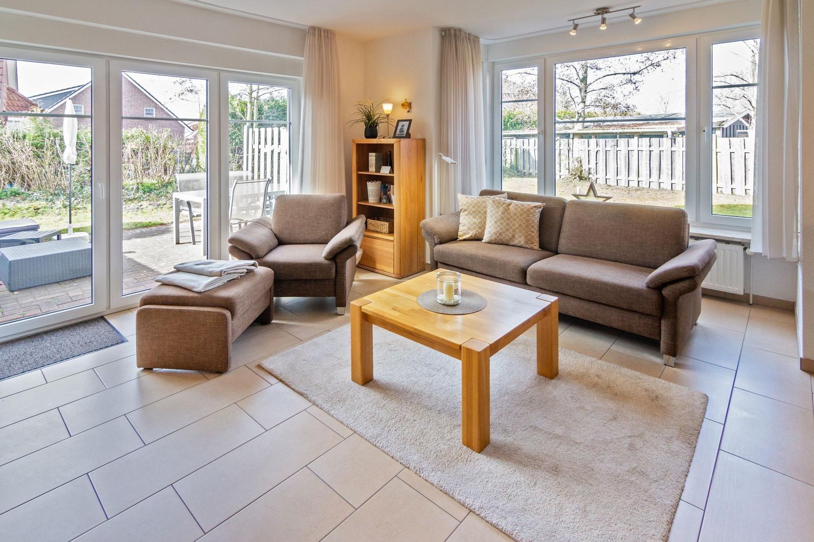Wohnzimmer mit Sofa, Sessel und Holztisch. Durchgänge zu Terrasse und Garten.