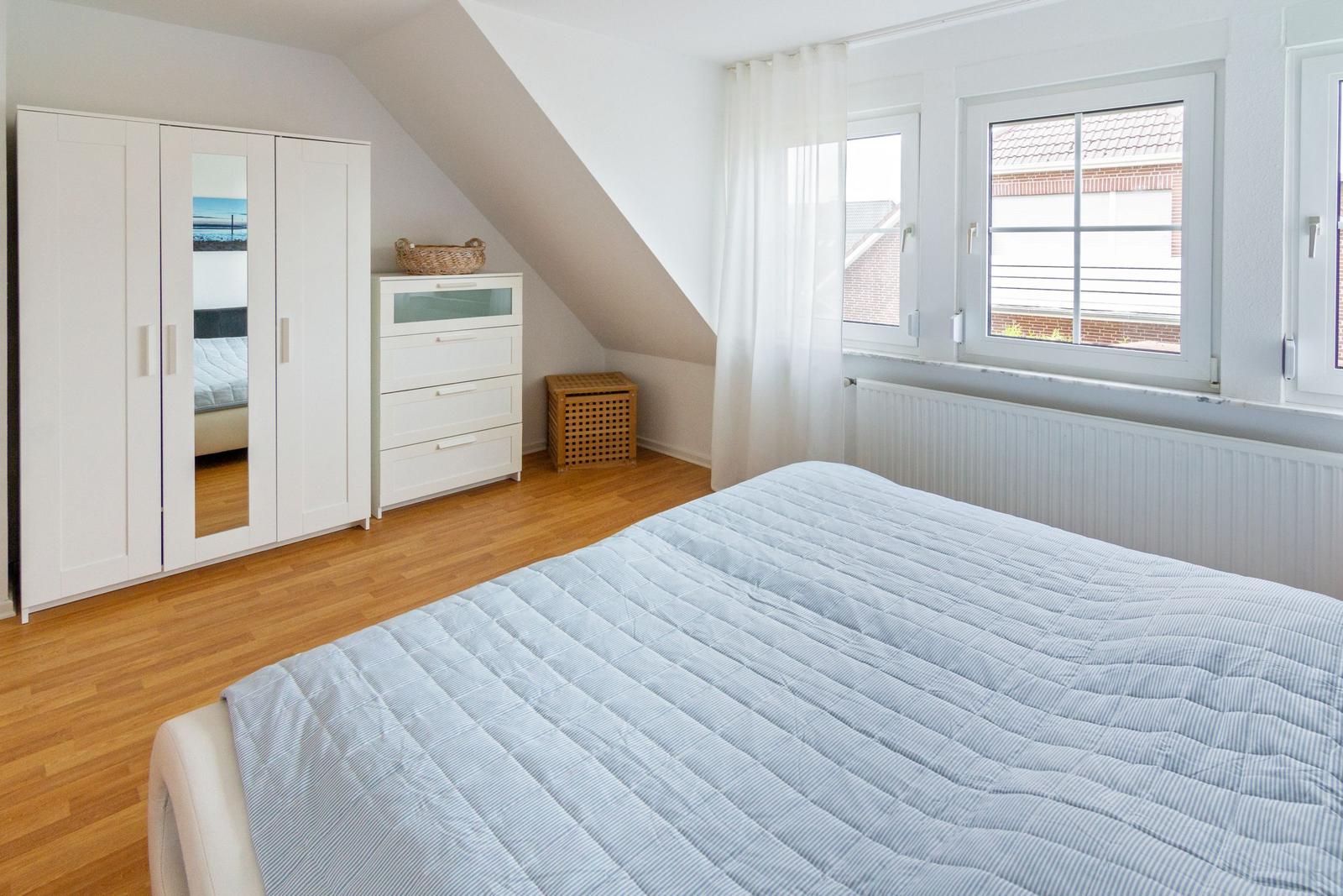Schlafzimmer mit Dachschrägen, Bett, Kleiderschrank und Fenster.