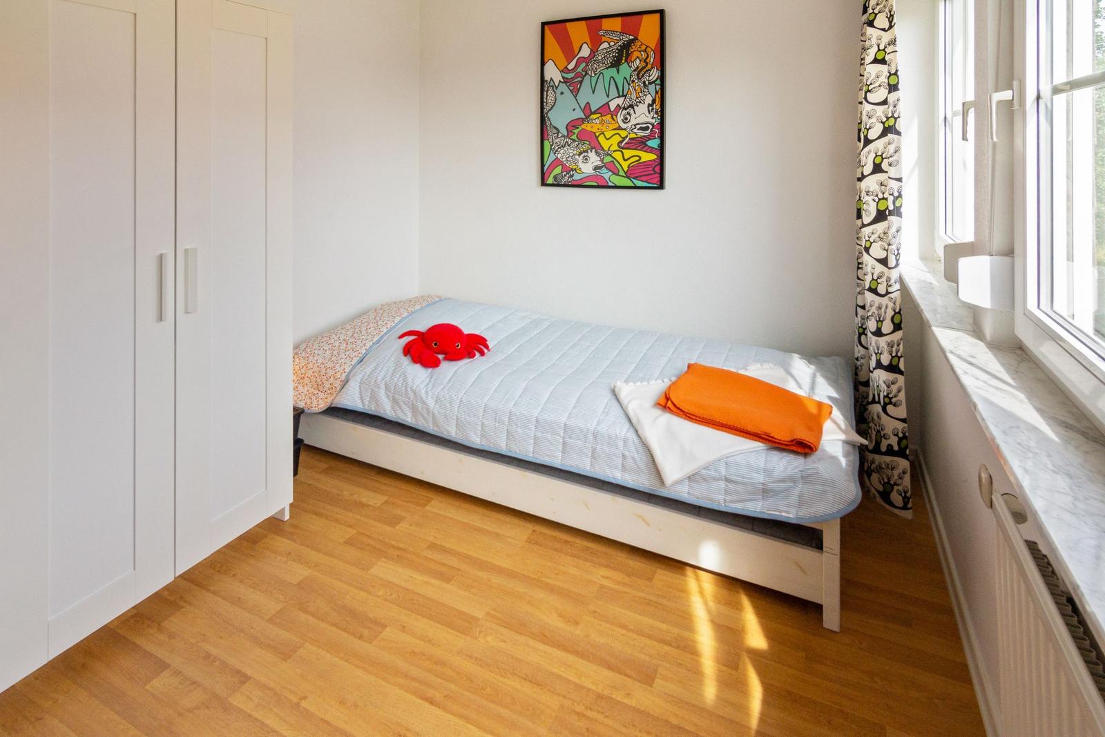 Ein Schlafzimmer mit Bett, Kleiderschrank und Fenster mit Vorhang.