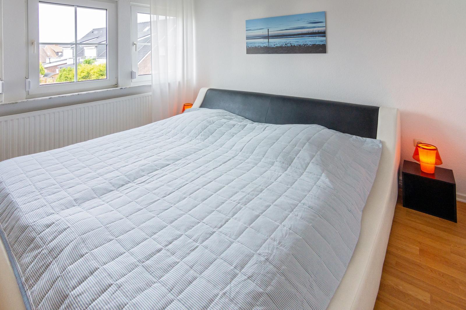 Schlafzimmer mit Doppelbett, Fenster und Nachttisch mit Lampe.