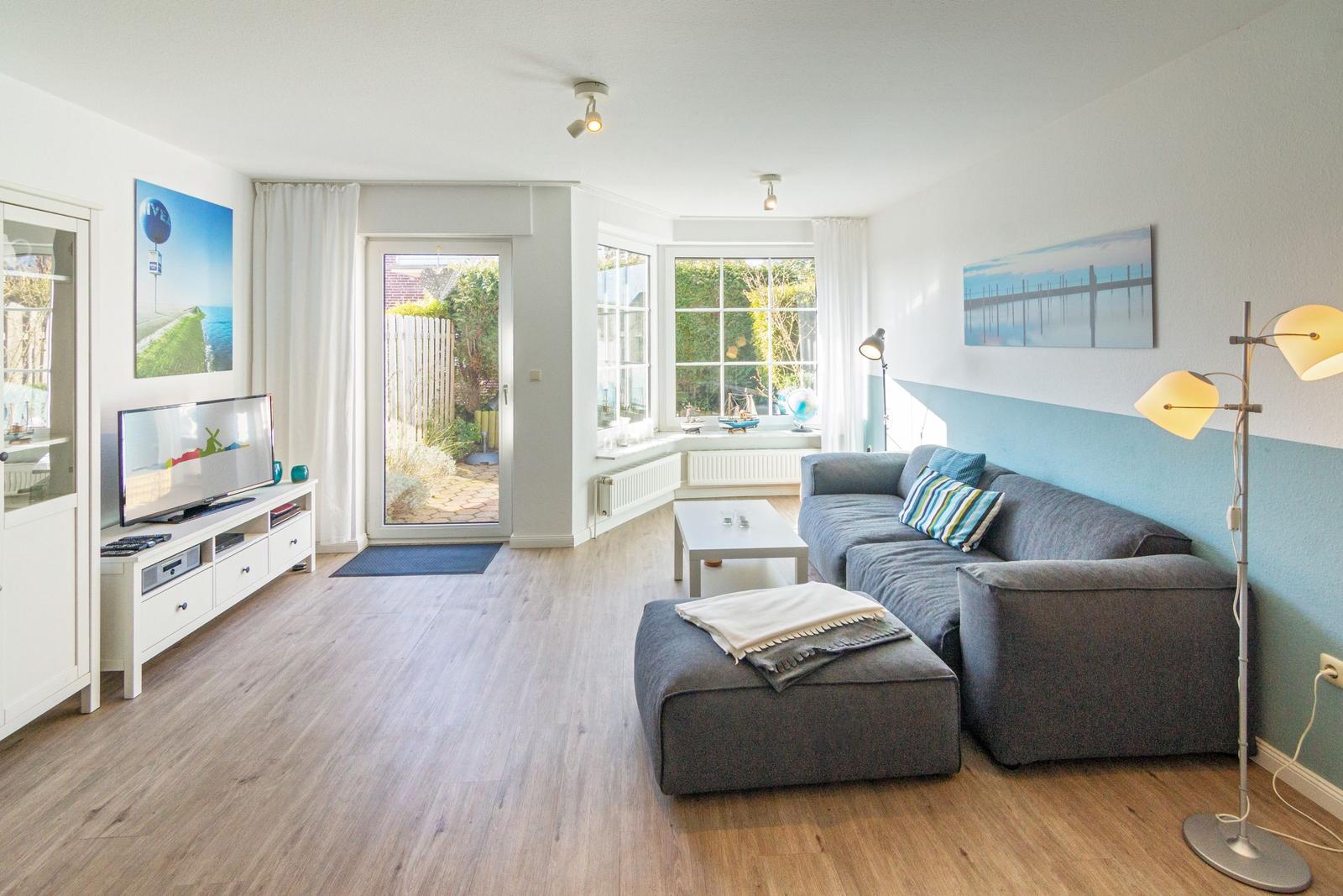 Wohnzimmer mit grauem Sofa, Fernseher und Blick auf Garten.
