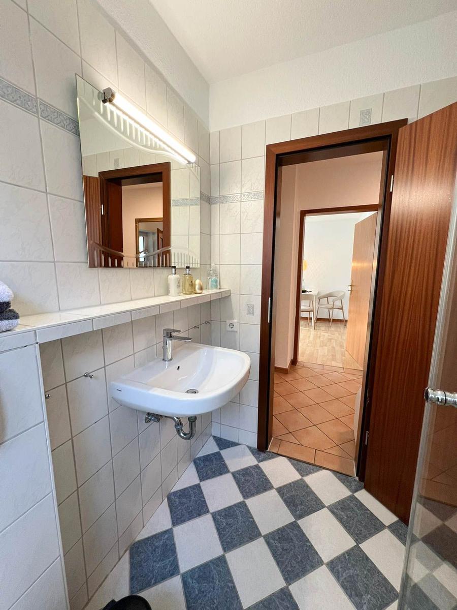 Badezimmer mit Waschbecken, Spiegel und schwarz-weißem Fliesenboden.