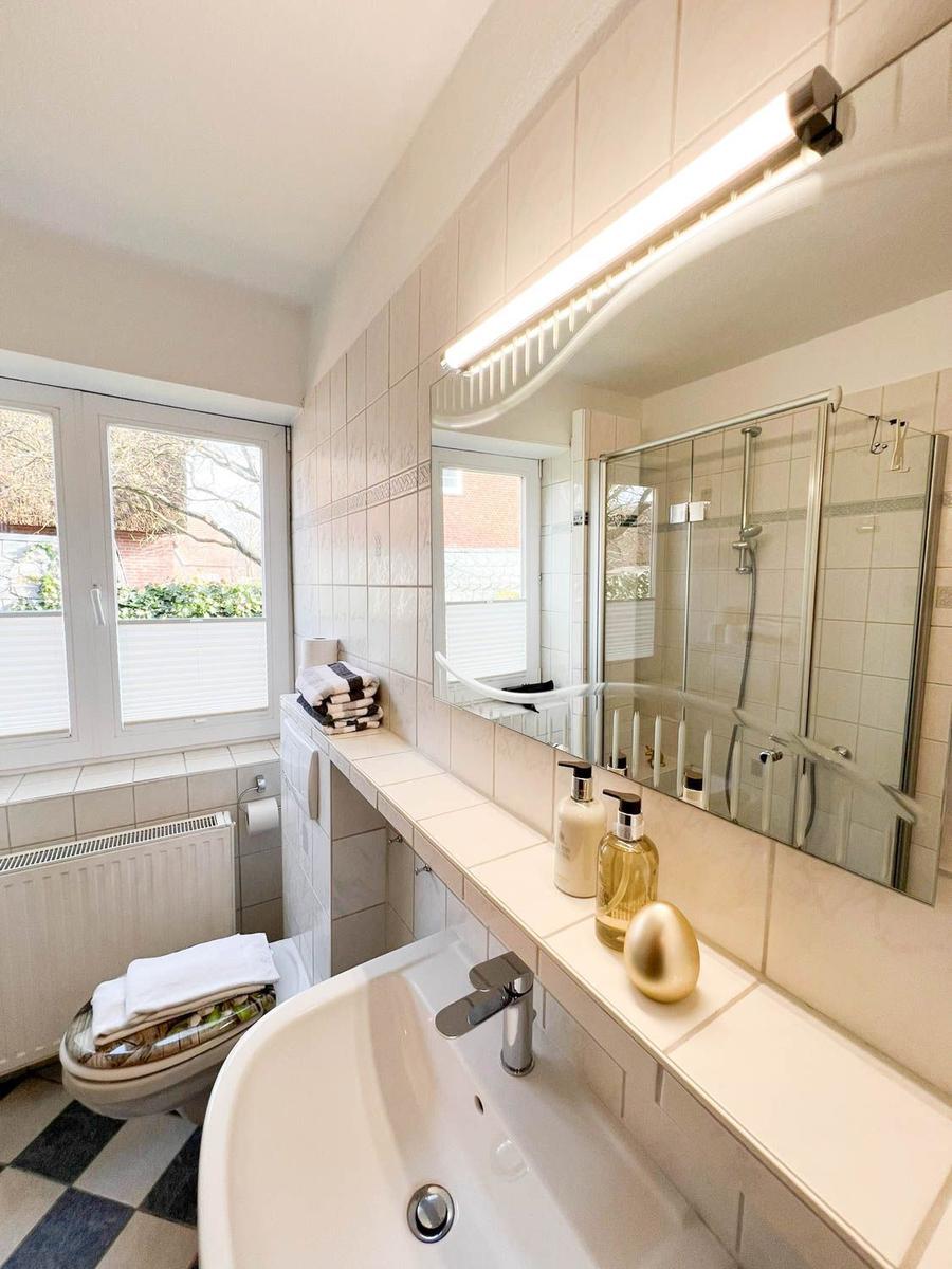Badezimmer mit Waschbecken, Spiegel, Dusche und Fenster.